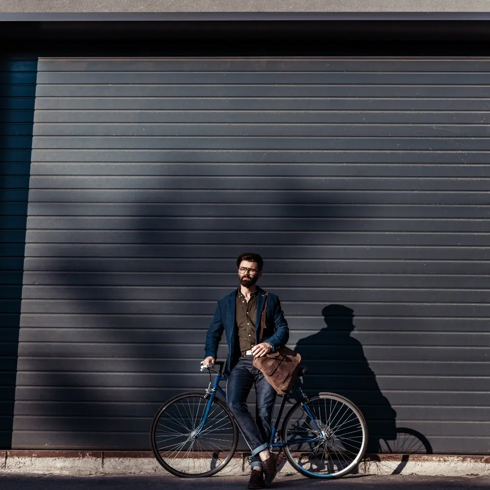 Man with a bicycle in front of a closed dark gray roll-down security shutter