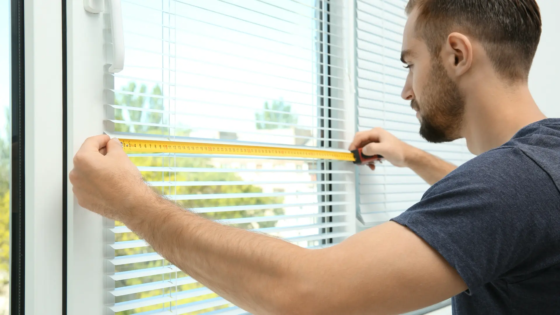 Technician measuring a window with a tape measure for new blinds