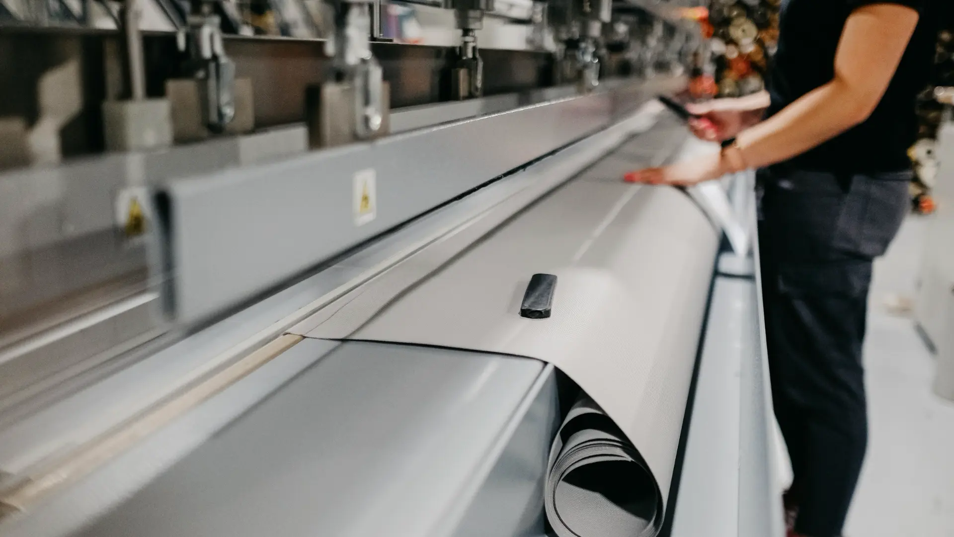 Worker feeding shade fabric through a cutting machine in a workshop