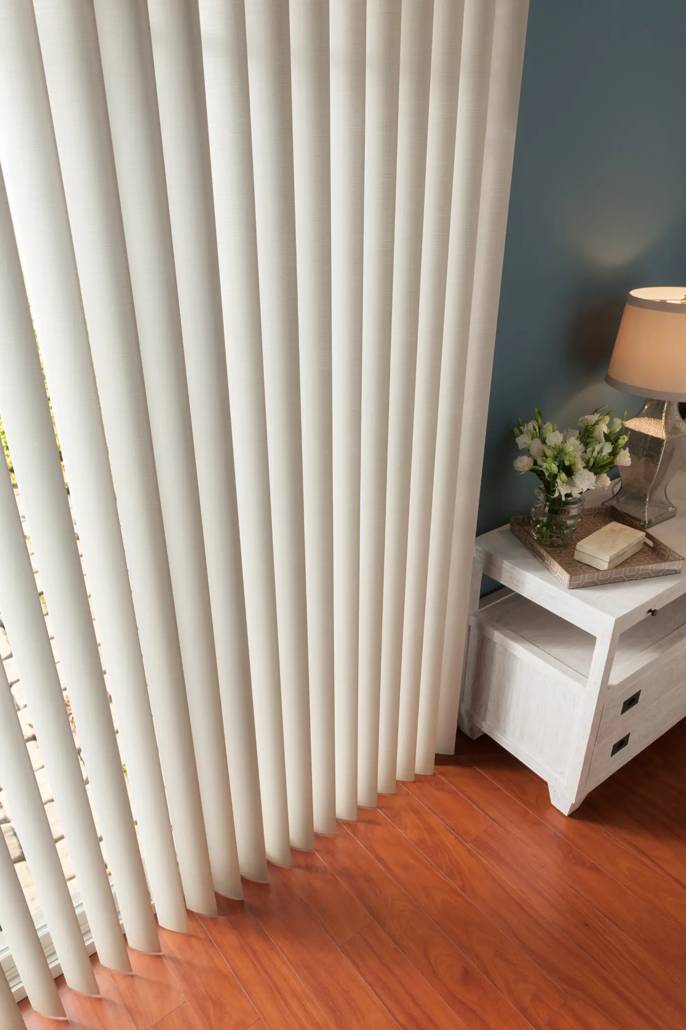 Close-up of white vertical blinds on a patio door beside a nightstand
