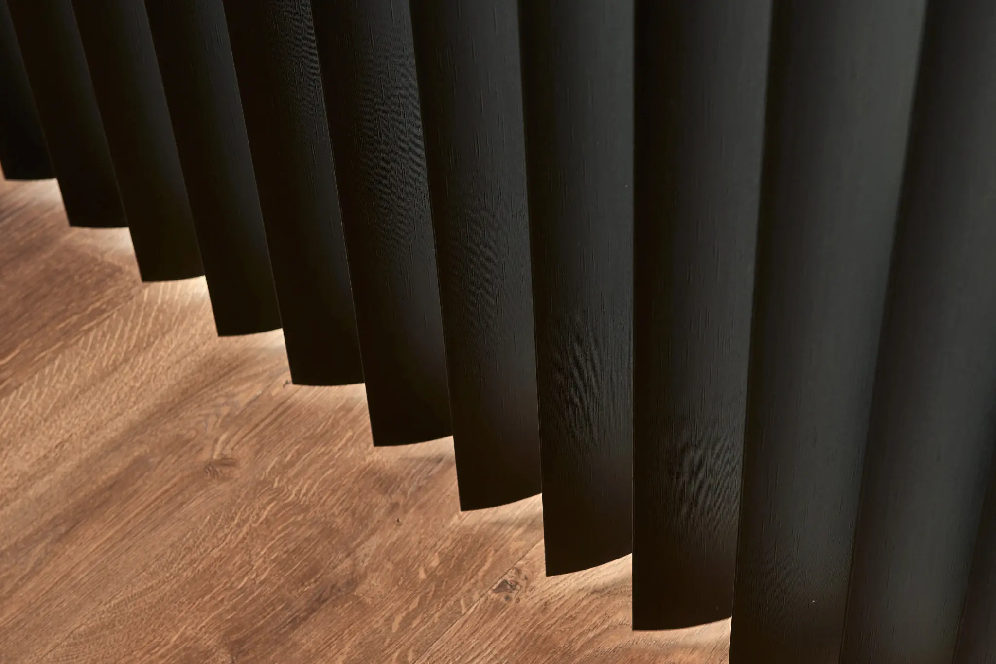 Close-up of black vinyl vertical blind vanes over a wood floor