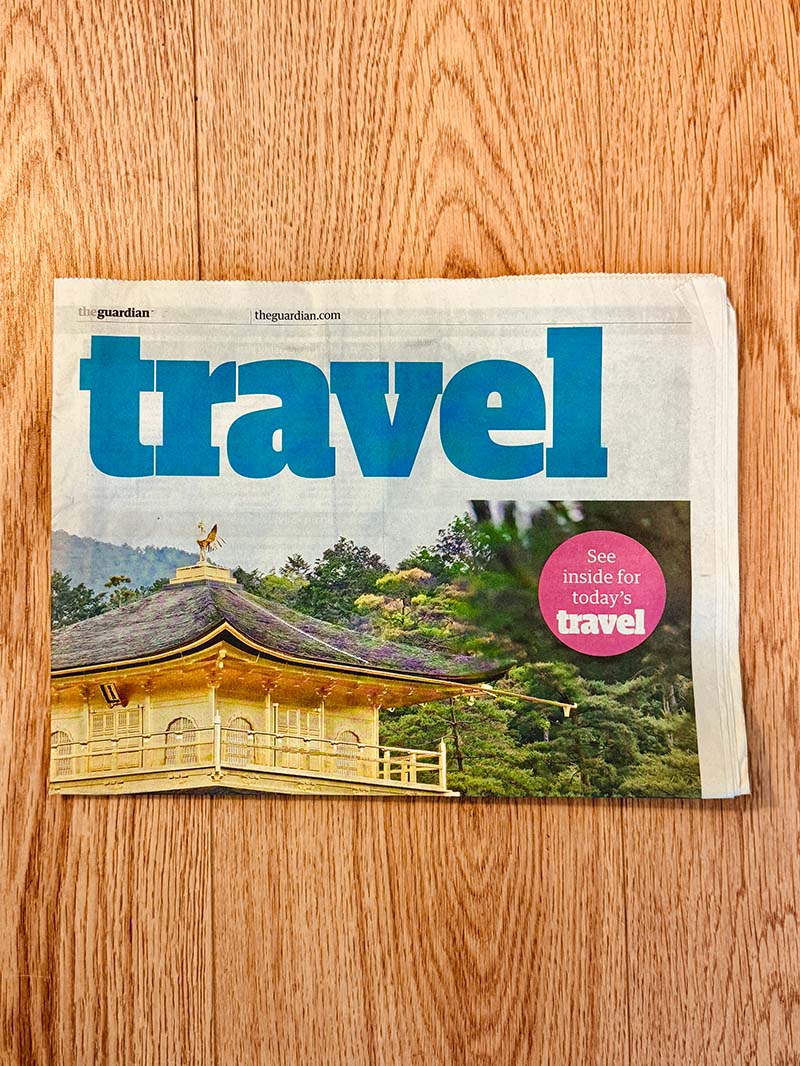Folded copy of The Guardian travel section showing a golden temple roof and trees on a wood floor.