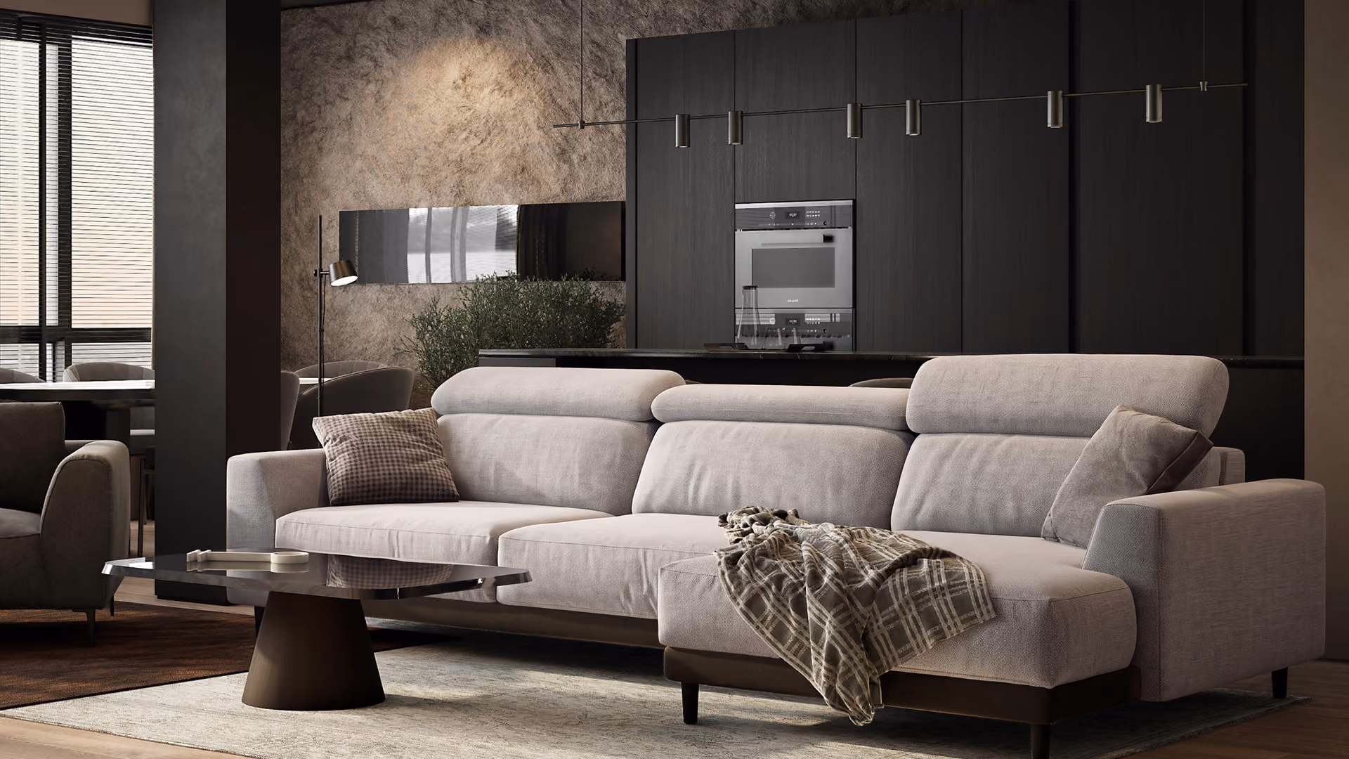 Modern living room with a light gray sectional sofa adorned with two pillows and a plaid throw blanket, a dark circular coffee table, and a decorated wall featuring dark cabinets and built-in ovens in the background.
