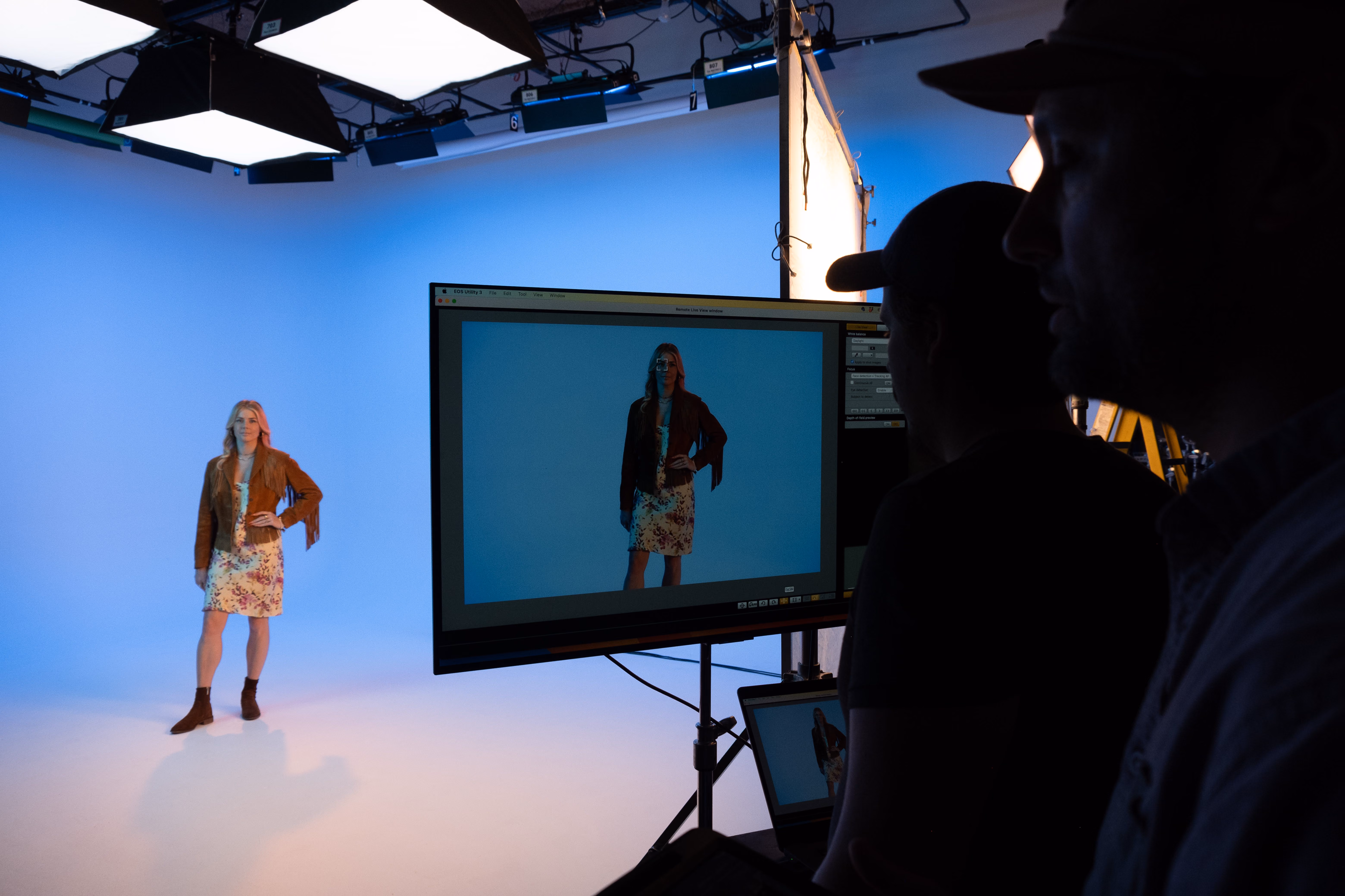 Model posing against a blue studio backdrop while crew watch the shot on a monitor