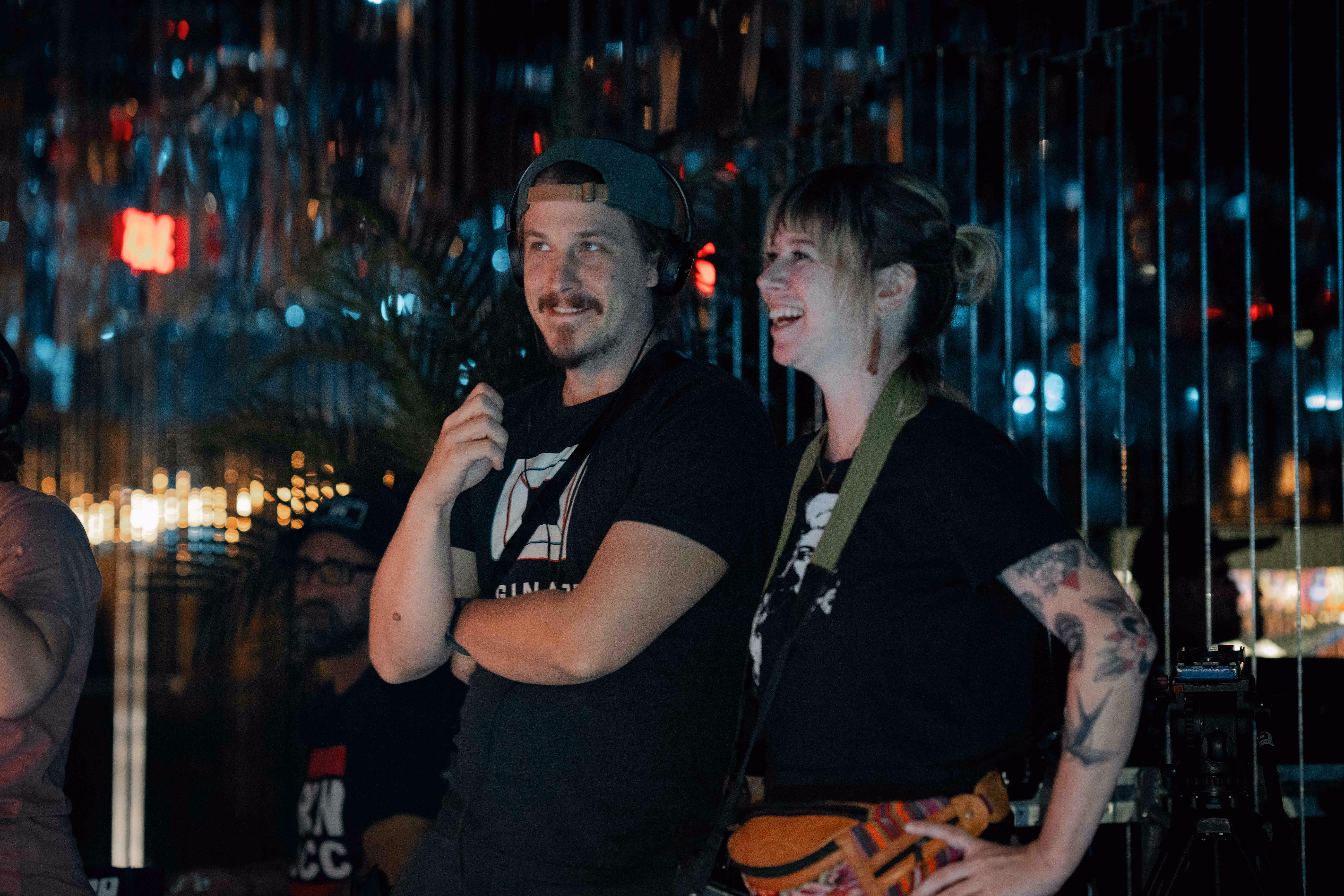Two crew members smiling while watching a shoot in a dimly lit bar