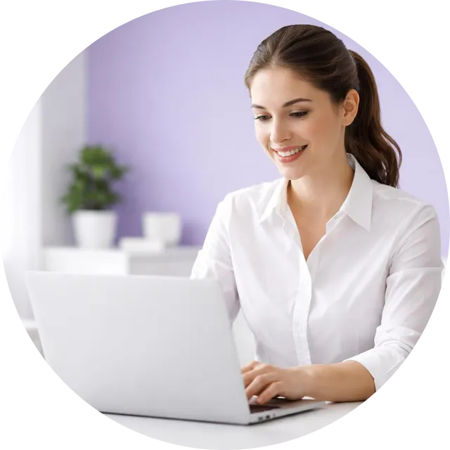 Smiling woman in a white shirt using a laptop in a room with a purple wall and a potted plant in the background.