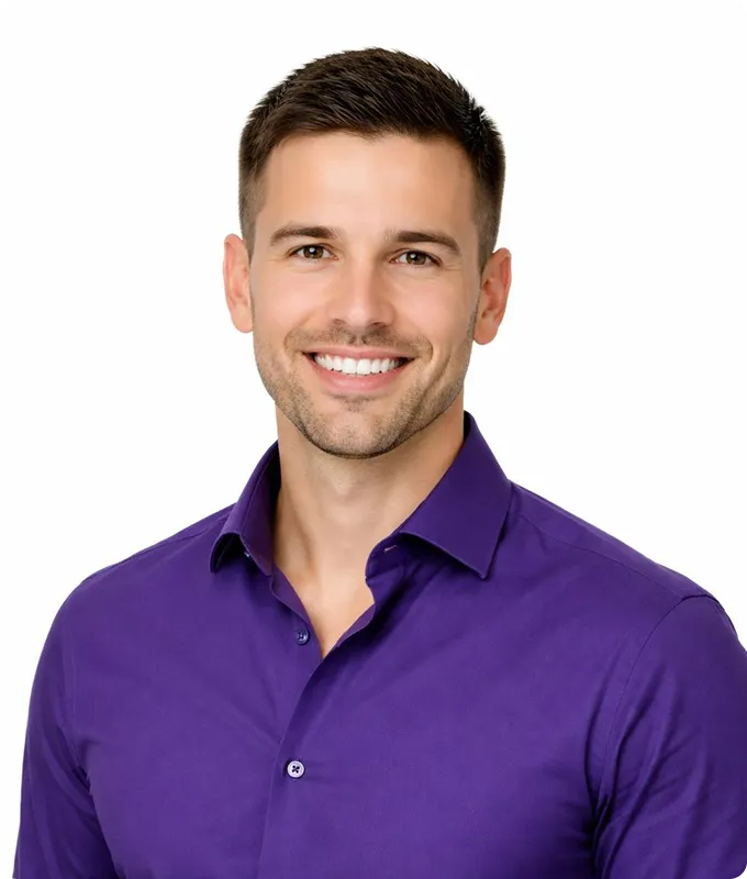 Smiling young man with short brown hair wearing a purple button-up shirt against a white background.