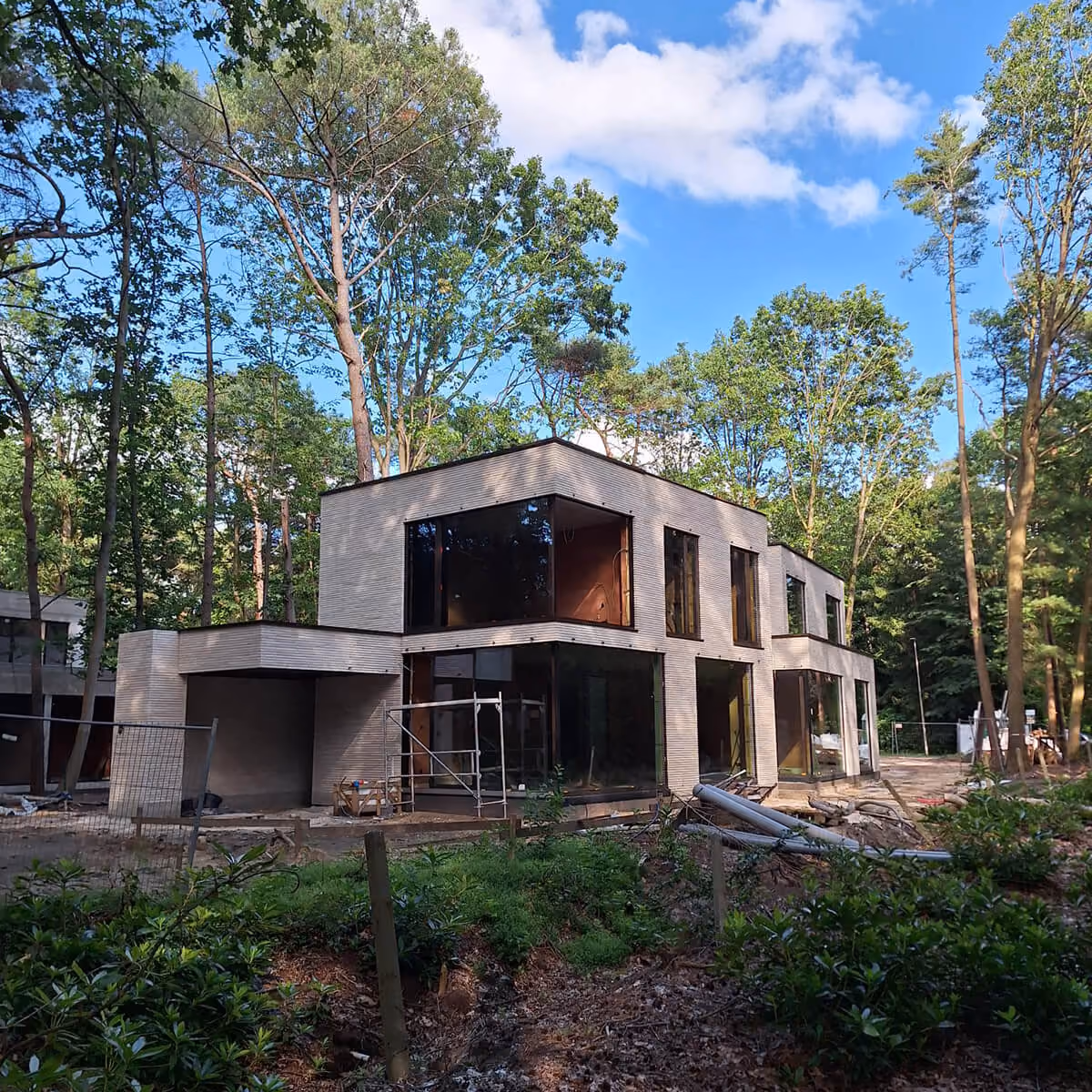 Moderne villa in aanbouw tussen de bomen, met grote glaspartijen en steigerwerk