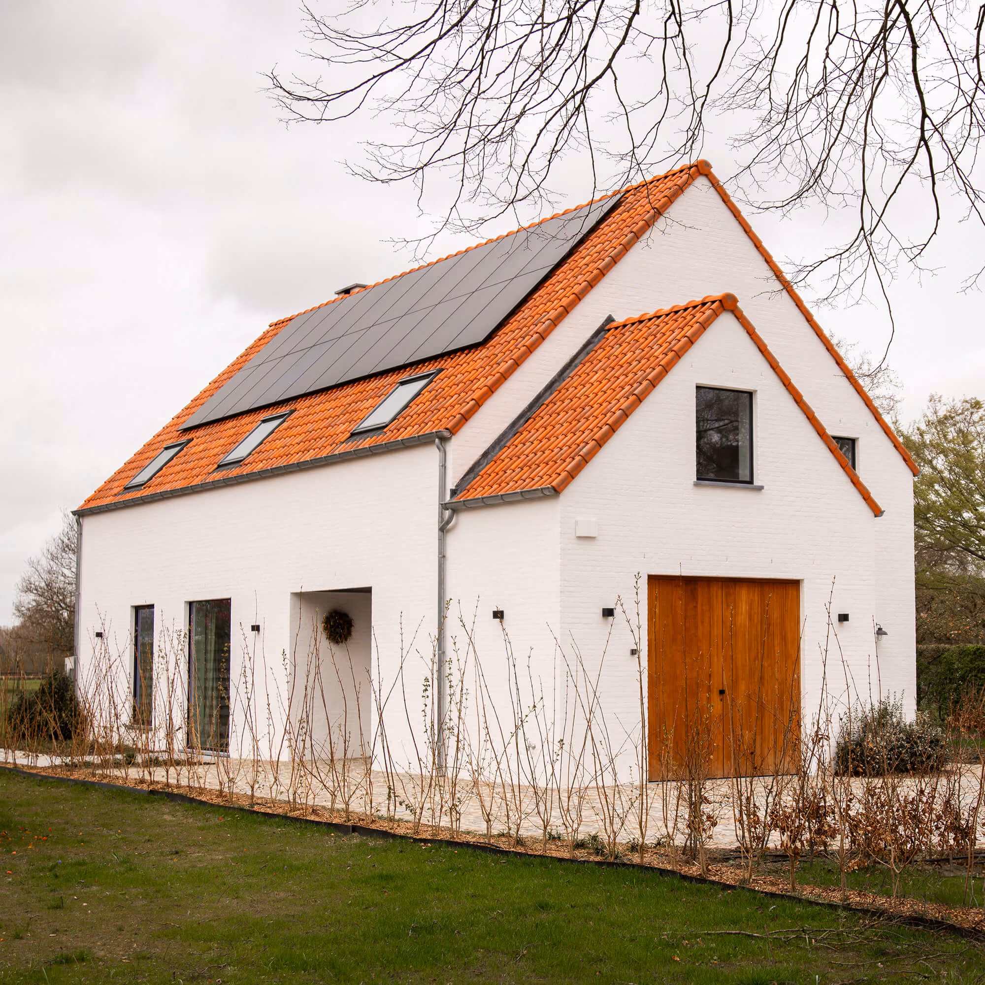 Witte hoeve met oranje pannendak, zonnepanelen en houten poortdeuren