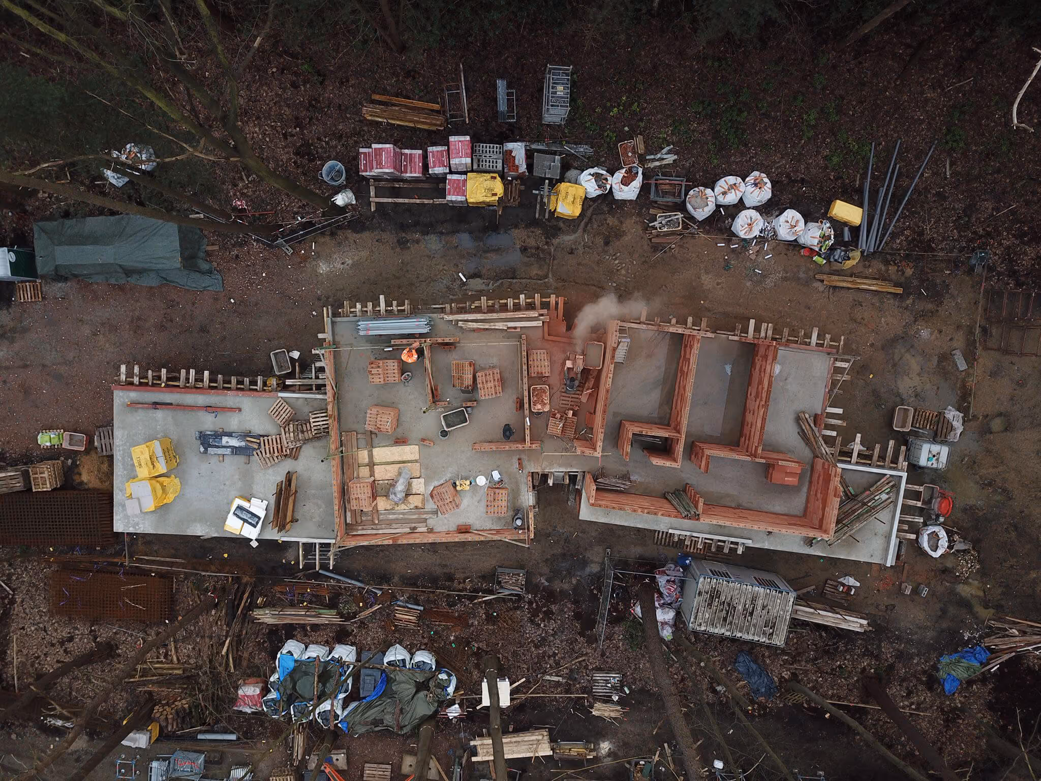 Luchtfoto van bouwplaats woningbouw in aanleg tussen bomen, met bakstenen muren, bouwmaterialen en steigers.