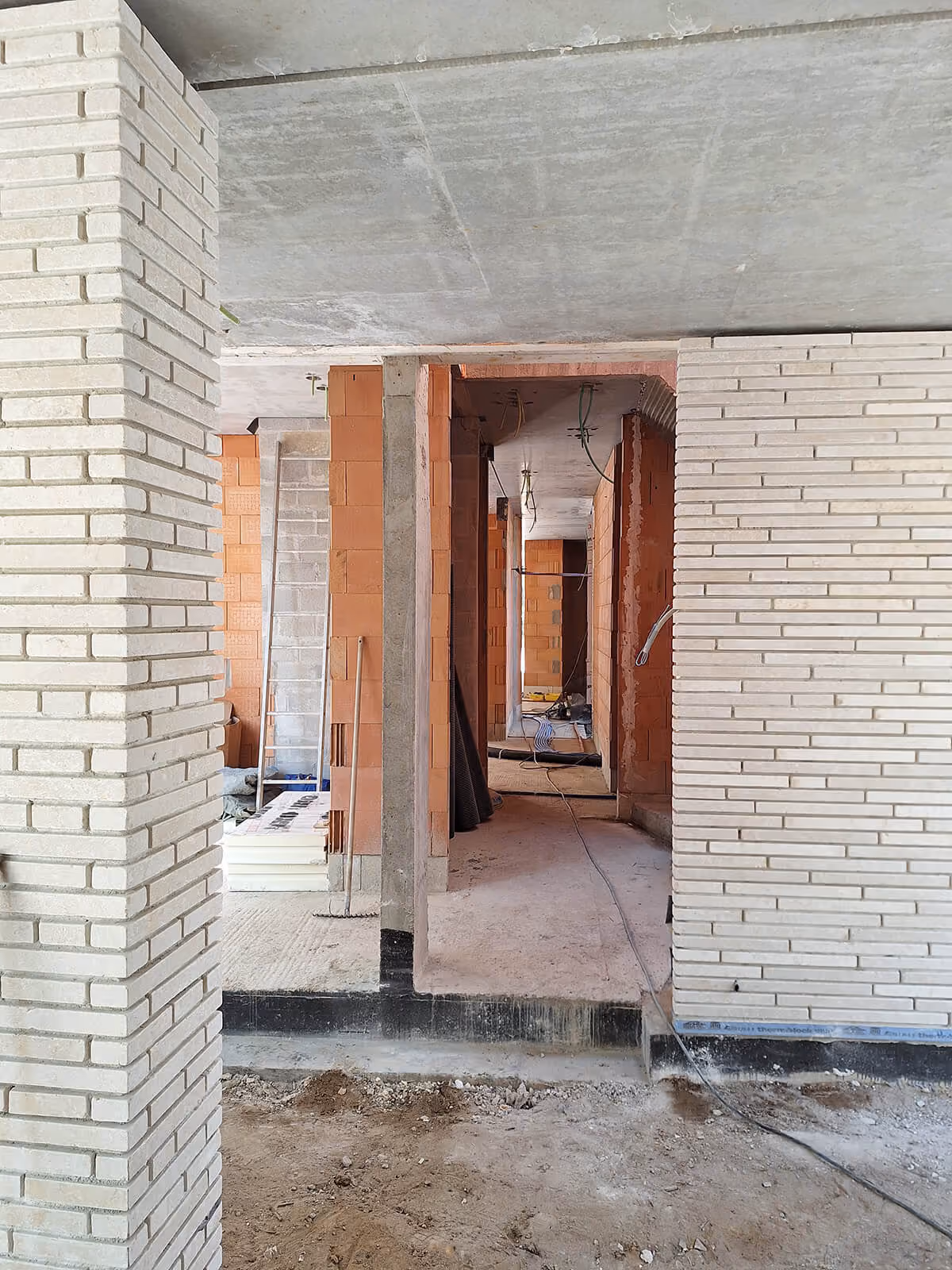 Doorkijk tussen bakstenen kolommen in ruwbouw van moderne woning.