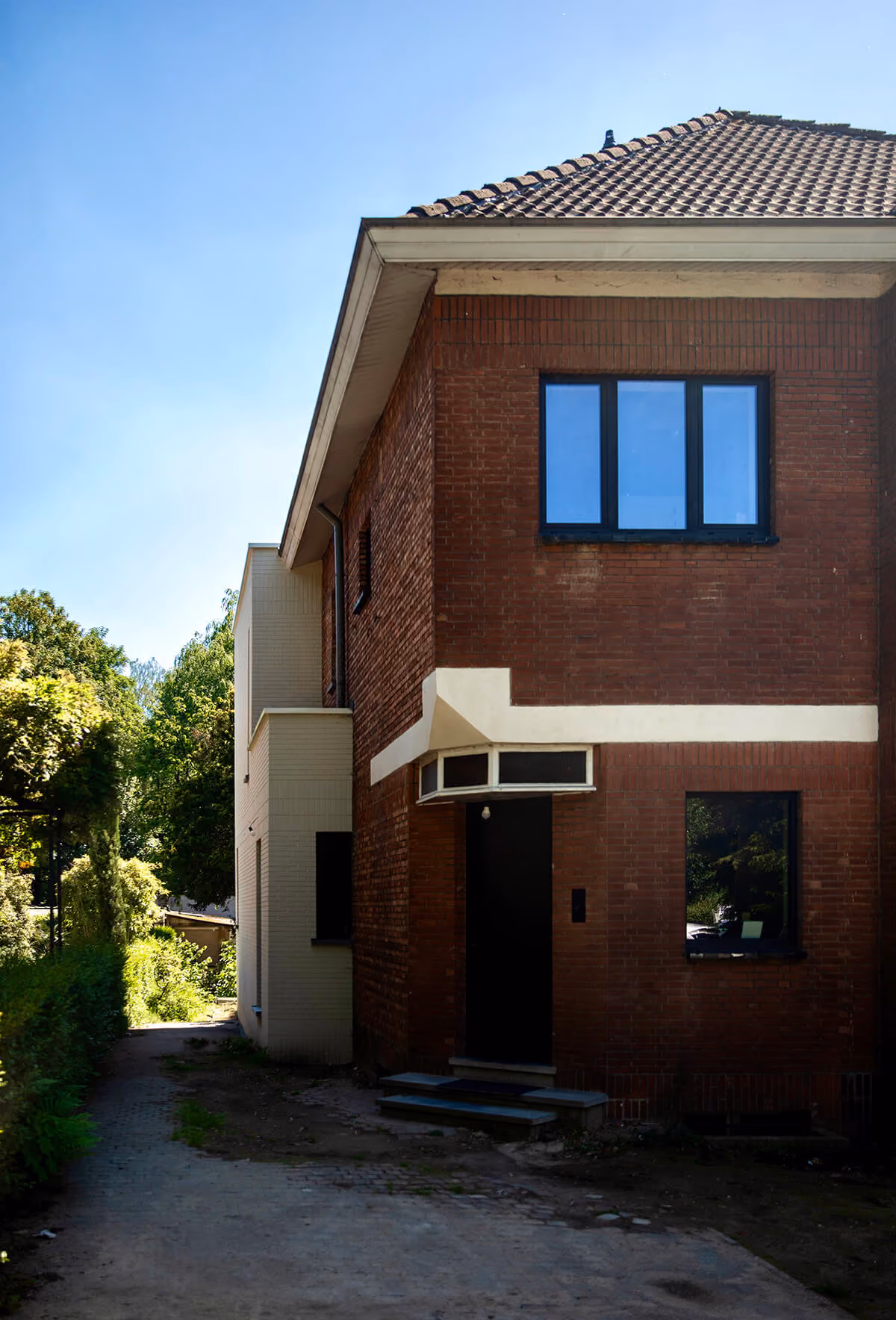 Zijaanzicht van bakstenen woning met zadeldak en witte aanbouw.