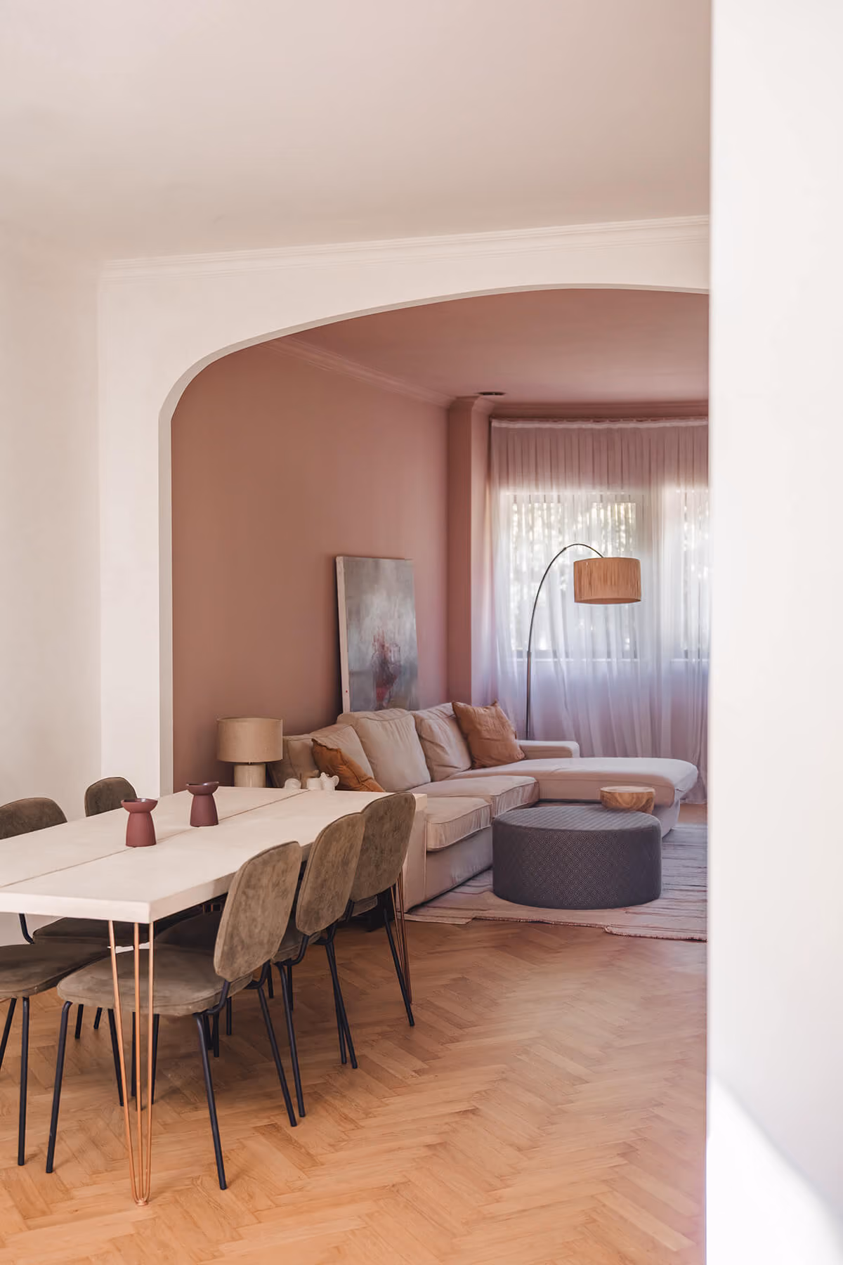 Woonkamer met visgraatparket, eettafel en zithoek in nis met roze wandkleur.