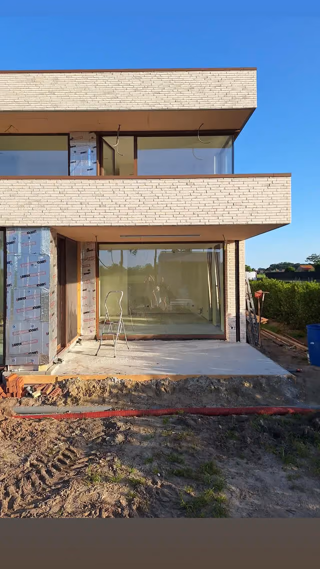 Moderne villa in aanbouw met lichte baksteengevel, grote schuifpui en nieuw aangelegd terras.