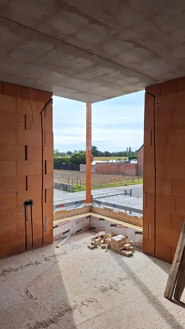 Hoekraam in aanbouw met zicht op open landschap, bakstenen binnenwanden nog onafgewerkt.