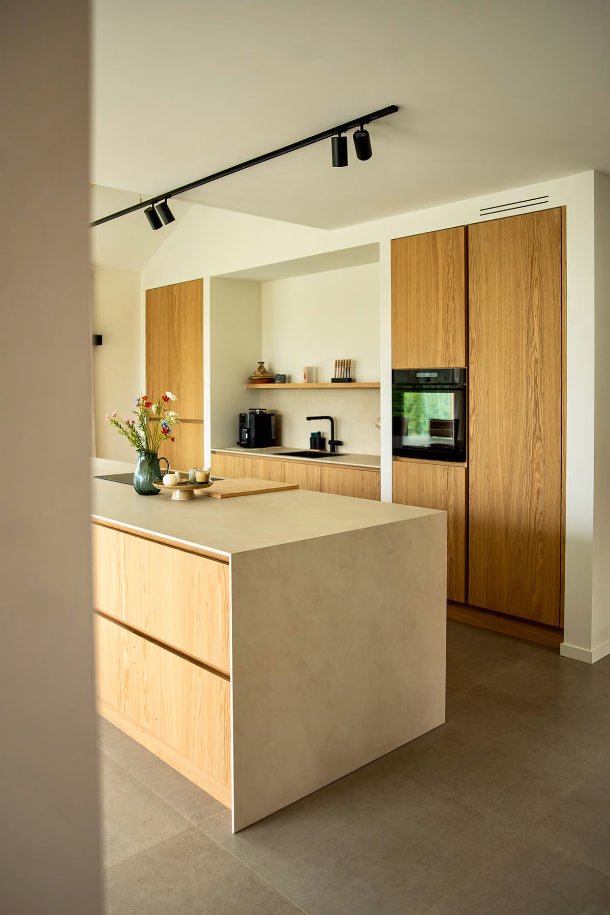 Keuken met eiken kastenwand, ingebouwde ovens en kookeiland met natuurstenen blad.