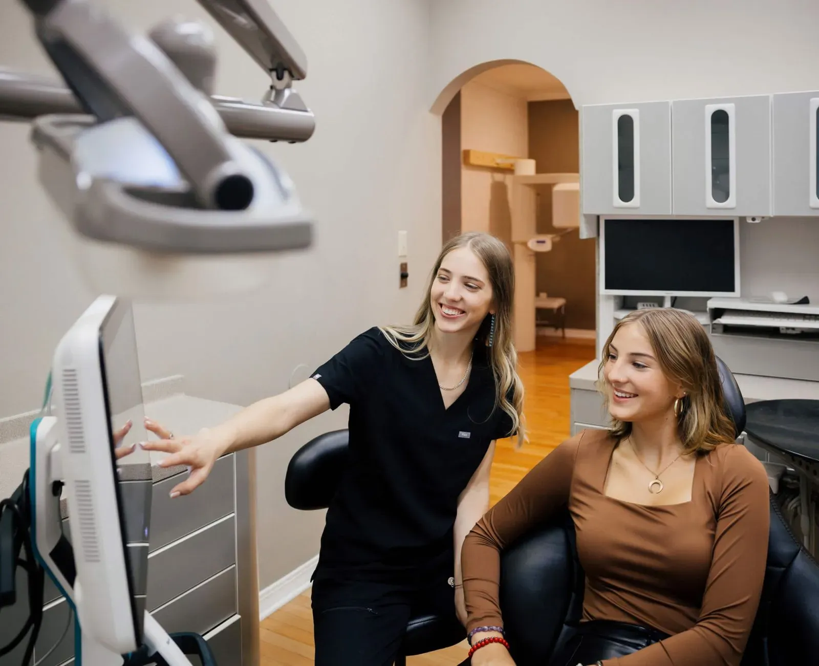 Dentist in black scrubs showing a smiling patient in brown top something on a screen in a dental office.
