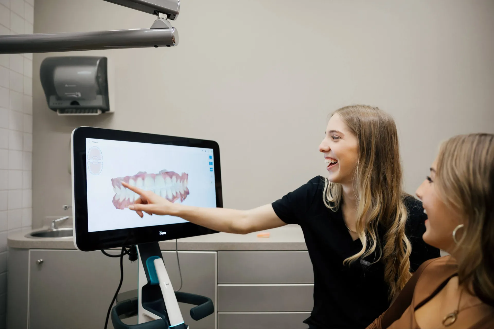 Dental professional showing a patient a 3D digital model of teeth on a screen in a clinic.