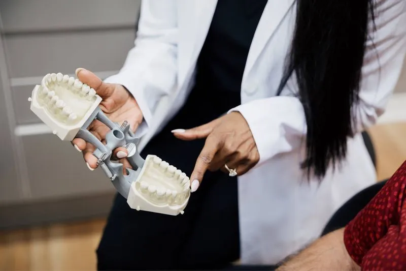 Dentist in white coat holding and pointing at a dental mold of upper and lower teeth.