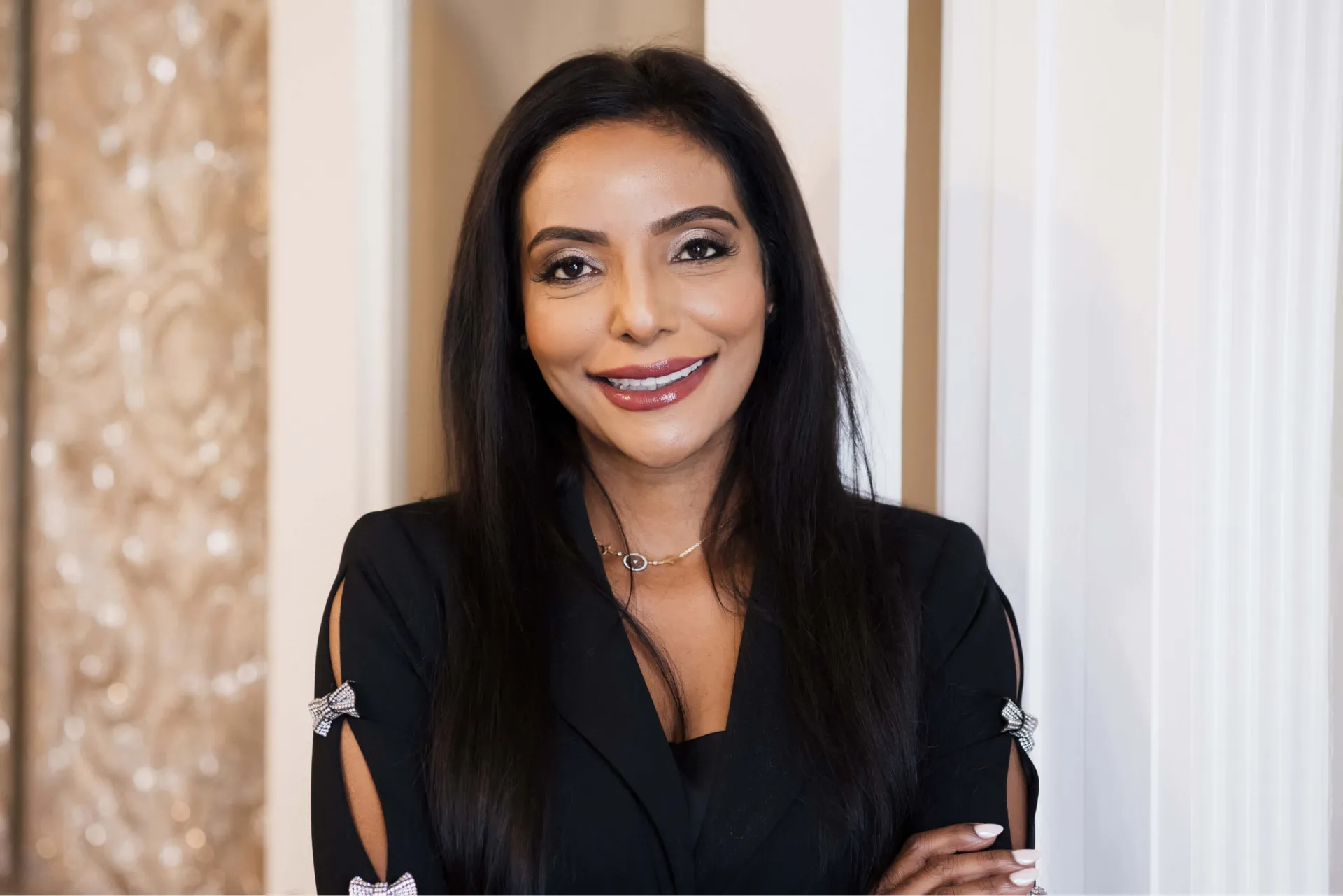 Smiling woman with long dark hair wearing a black outfit with bow accents on sleeves.