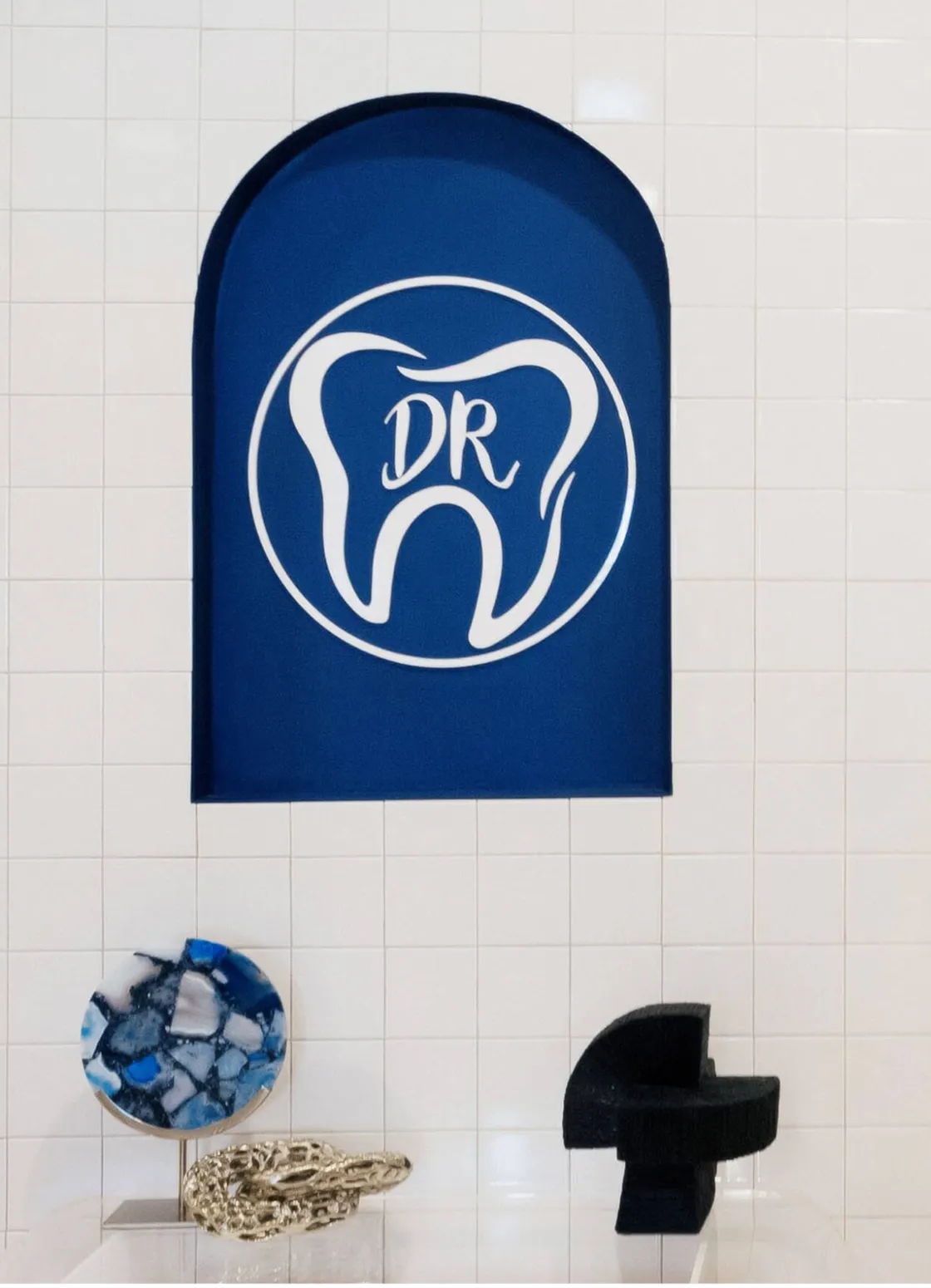Blue wall sign shaped like a tooth with letters 'DR' above blue, gold, and black abstract sculptures.
