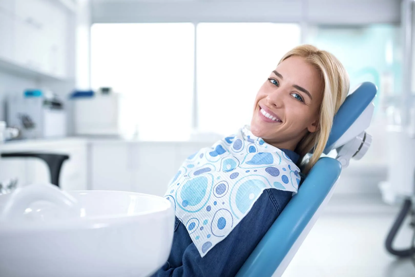 Smiling woman reclined in a dental chair with a bib in a bright dental clinic.