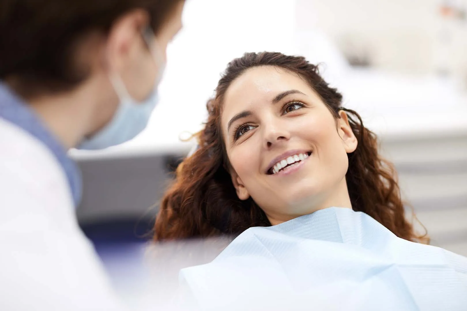 Smiling woman reclined in a dental chair looking at a masked dentist.