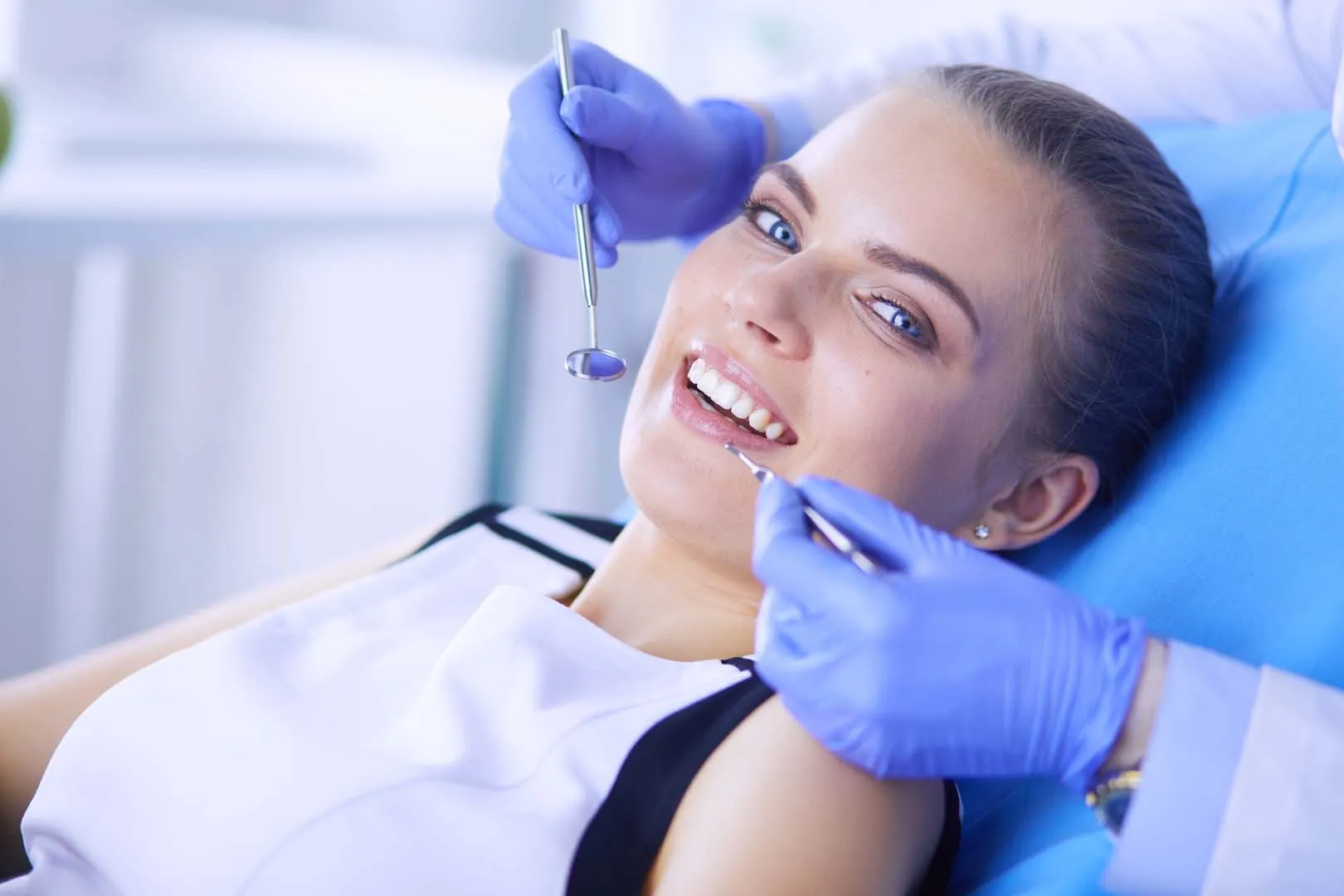 Smiling woman lying back during a dental checkup with a dentist holding dental tools near her mouth.