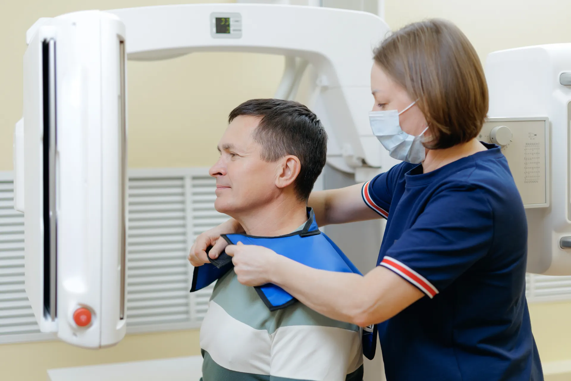 Healthcare worker fitting protective lead apron on man before X-ray imaging procedure.