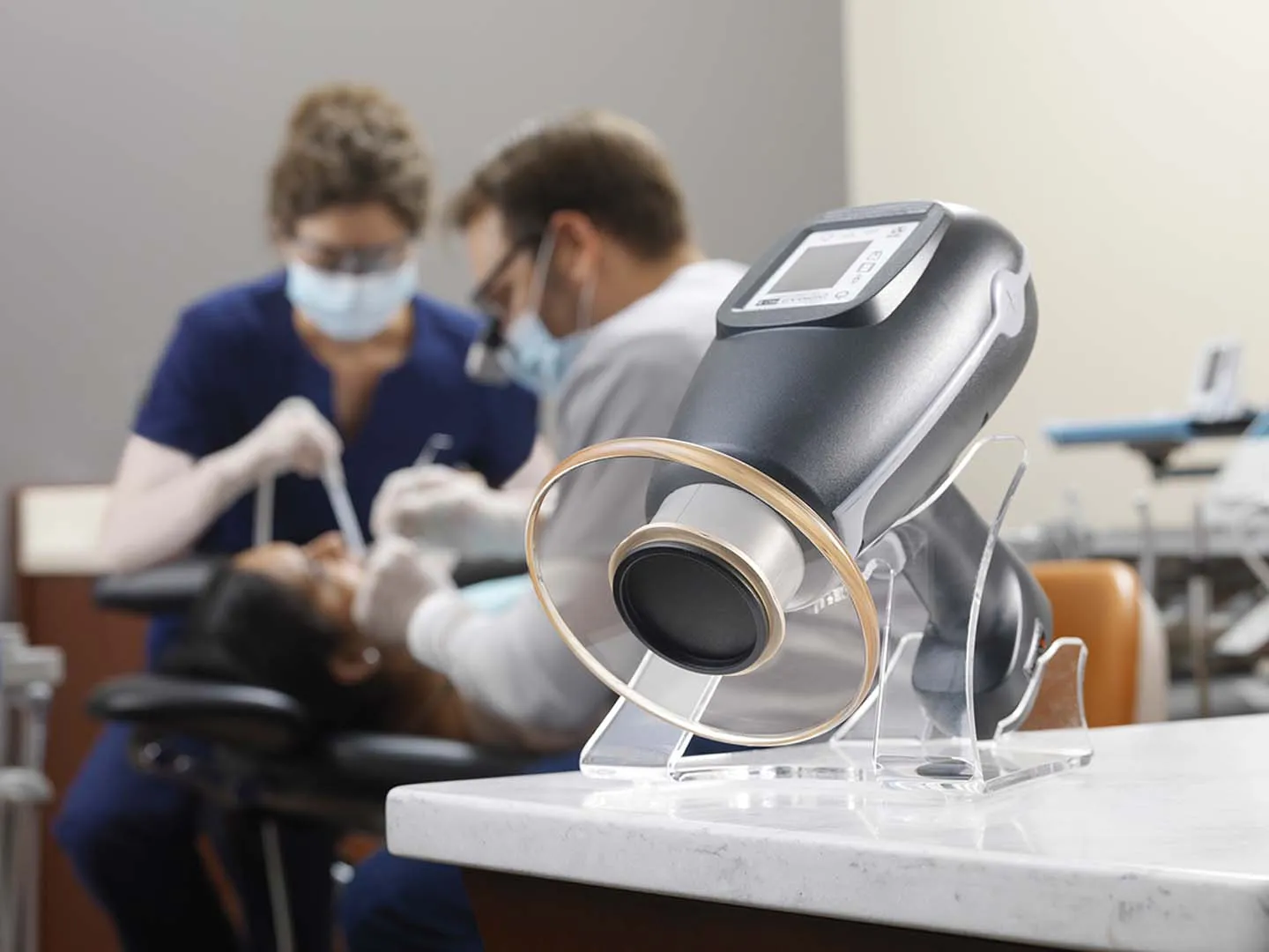 Dental office with suction device in foreground and dentists treating a patient in the background.