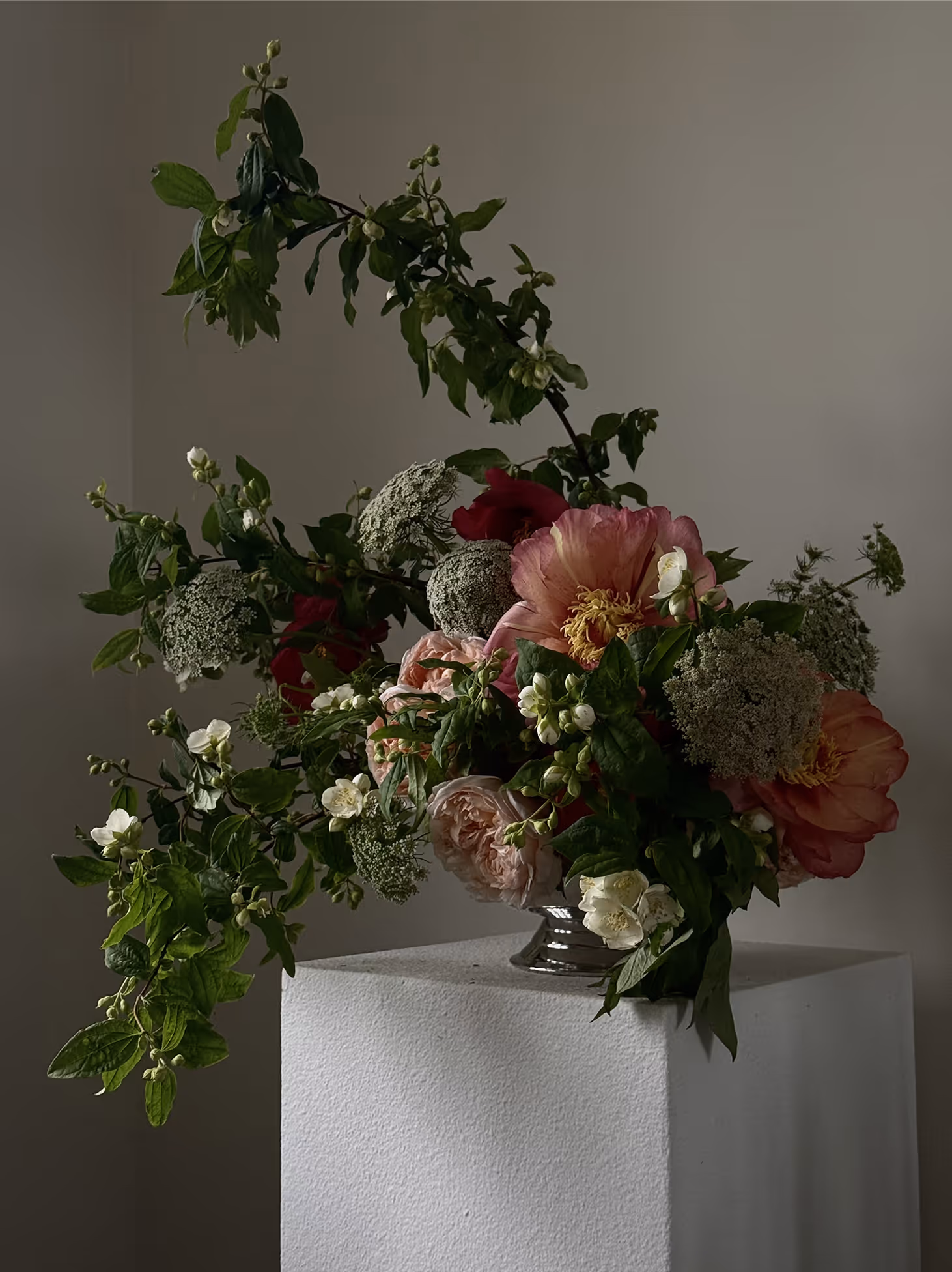 Floral arrangement with pink, white, and red flowers and green foliage on a white pedestal.