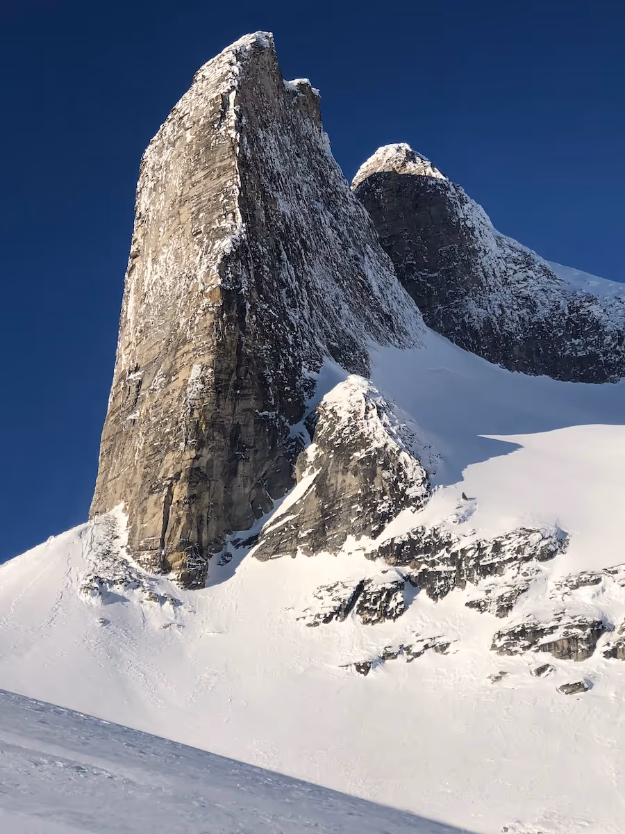 Tall, steep rocky mountain peak covered partially with snow under a clear blue sky. gimli ski touring valhallas