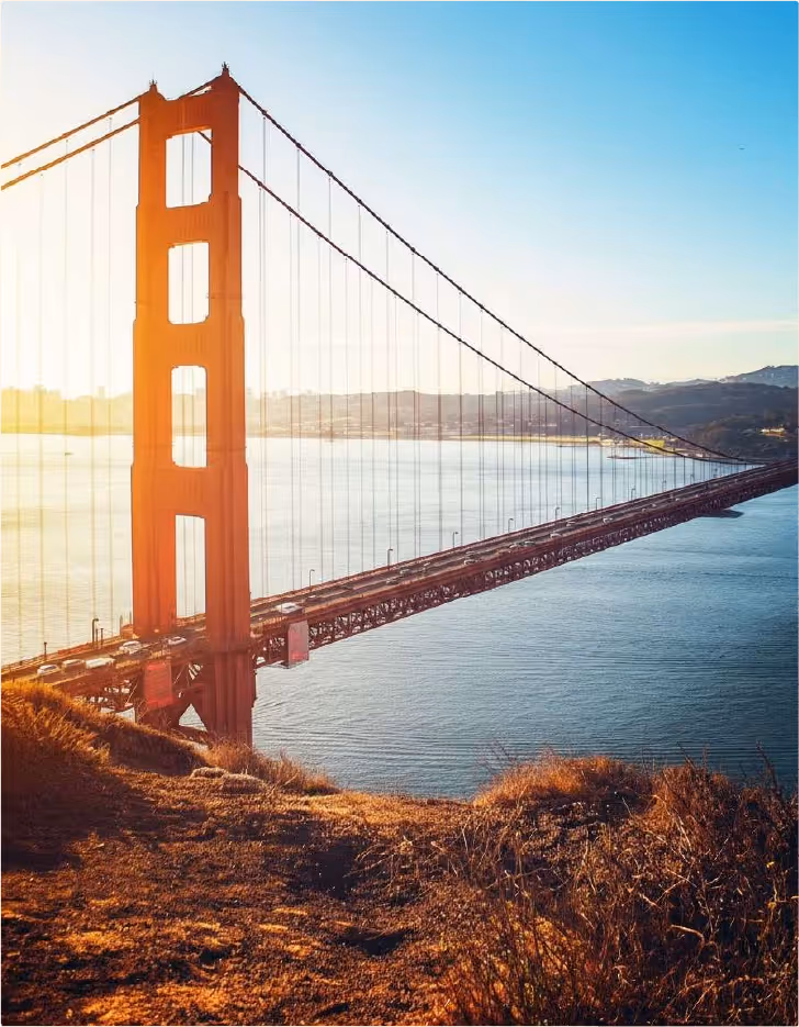 Golden Gate Bridge spanning blue water with hills in the background at sunset.