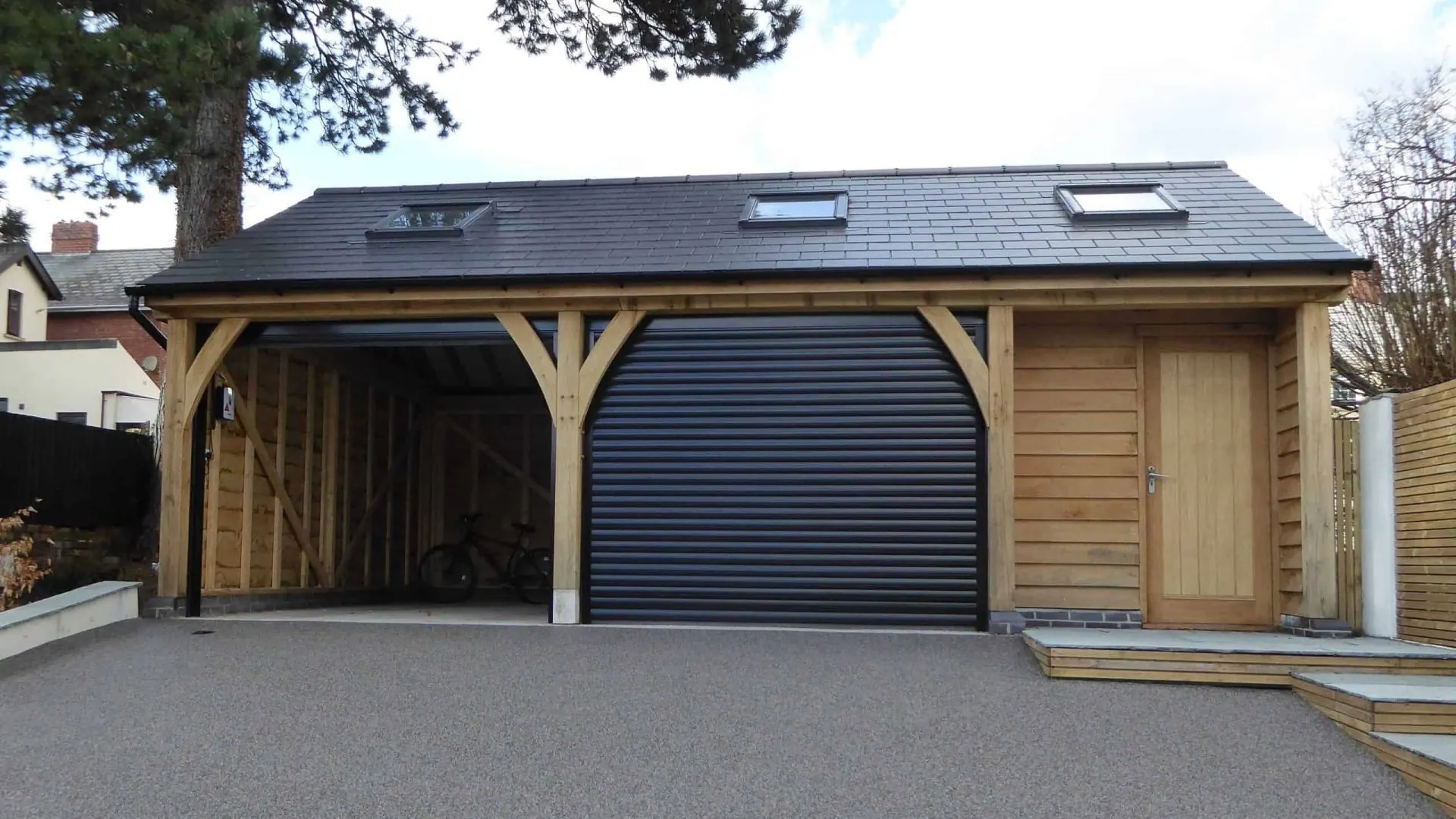 The oak frame garage at Caerleon: a roller-door bay with the gym bay beside it, under a slate roof.