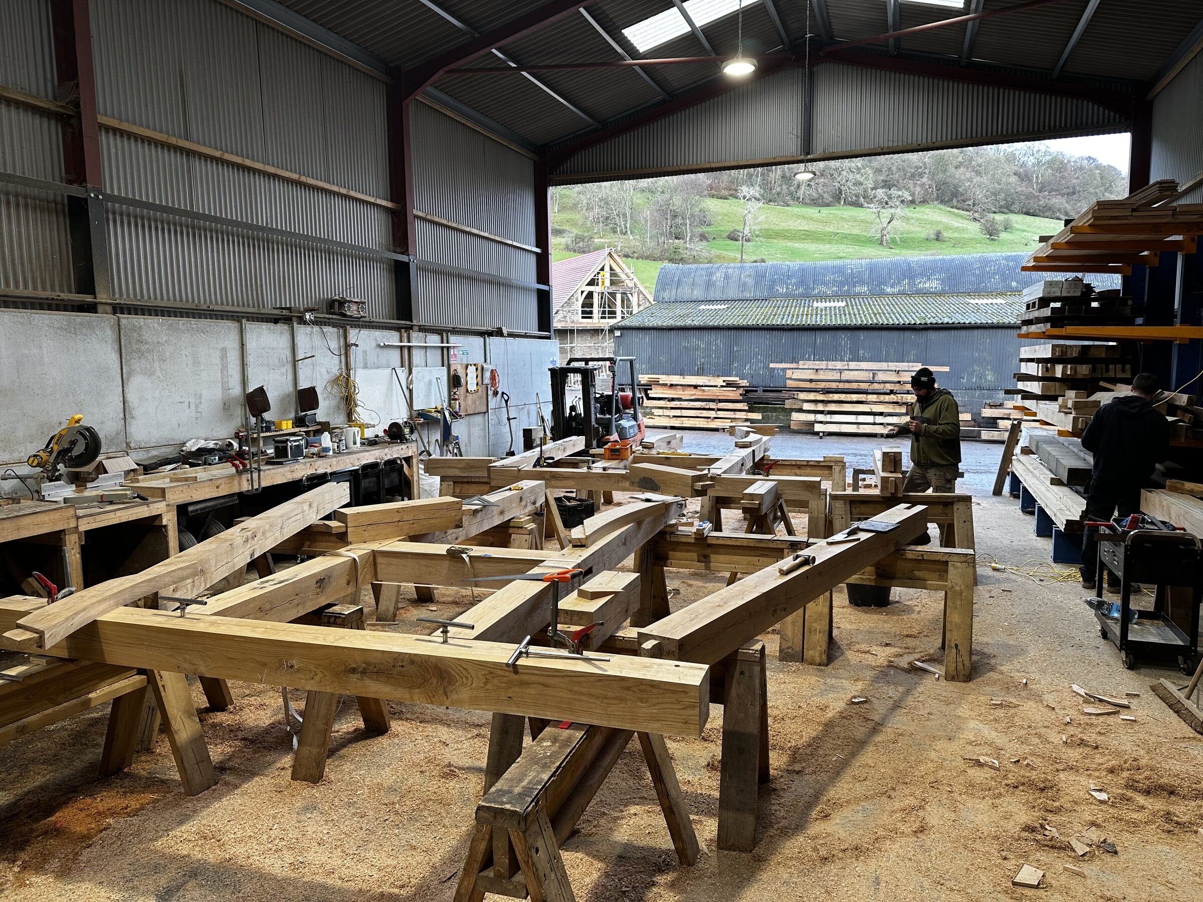 Oak roof frames laid out on trestles in the Foxtail Oak workshop near Abergavenny, with two of the team at work and the yard doors open.