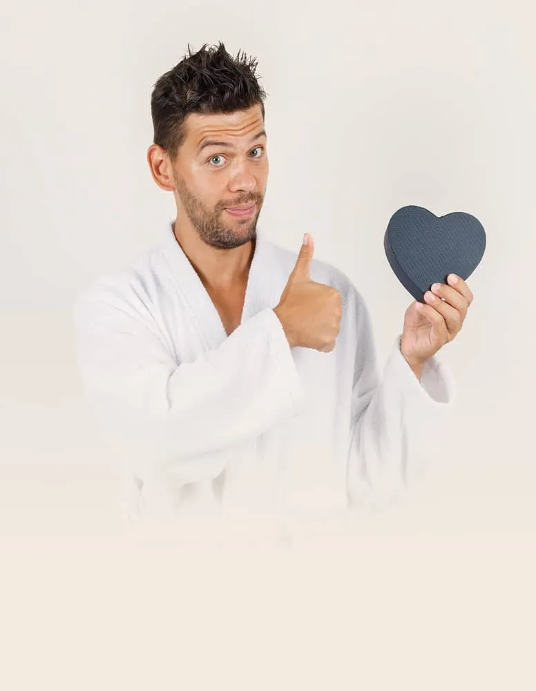 Man in white robe holding heart-shaped object and giving thumbs up with a confident expression.