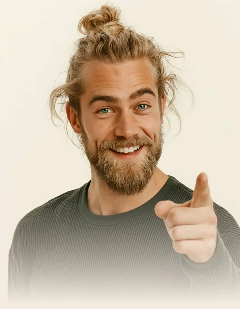Smiling man with blonde hair in a bun pointing forward wearing a green sweater.