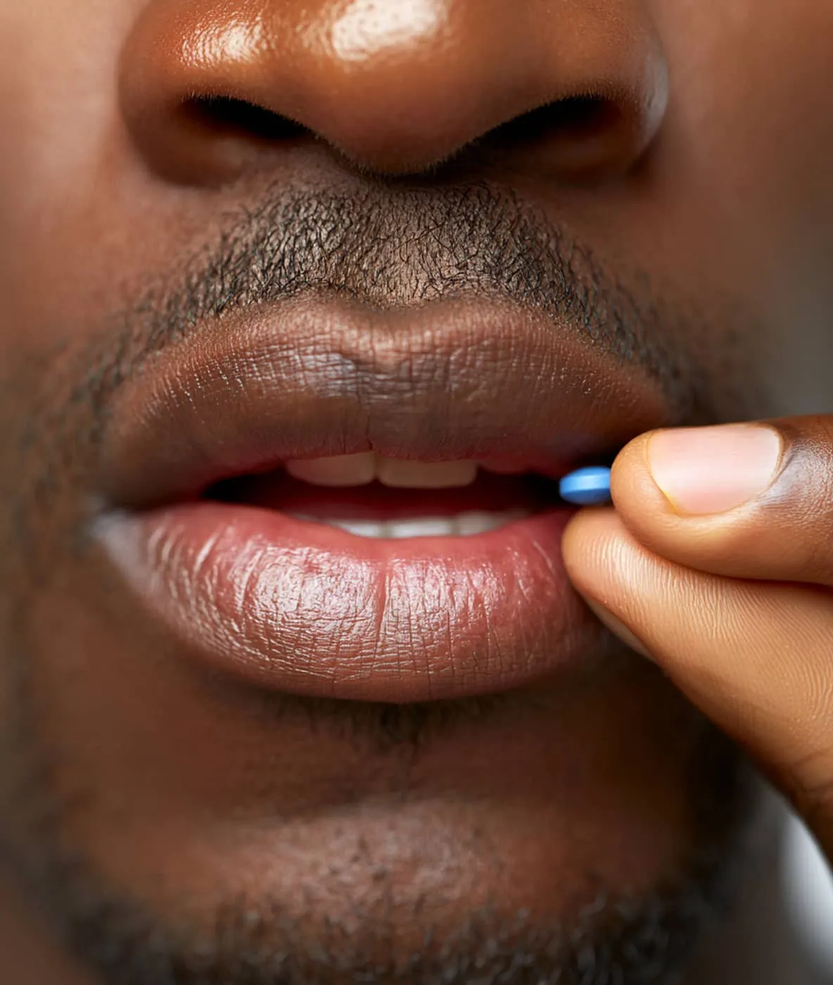 Close-up of a person holding a small blue pill near their slightly open mouth.