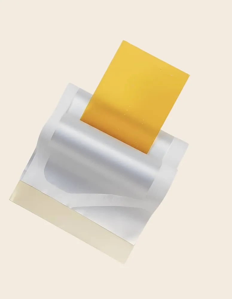Silver adhesive tape with a yellow sticky strip partially peeled off against a beige background.