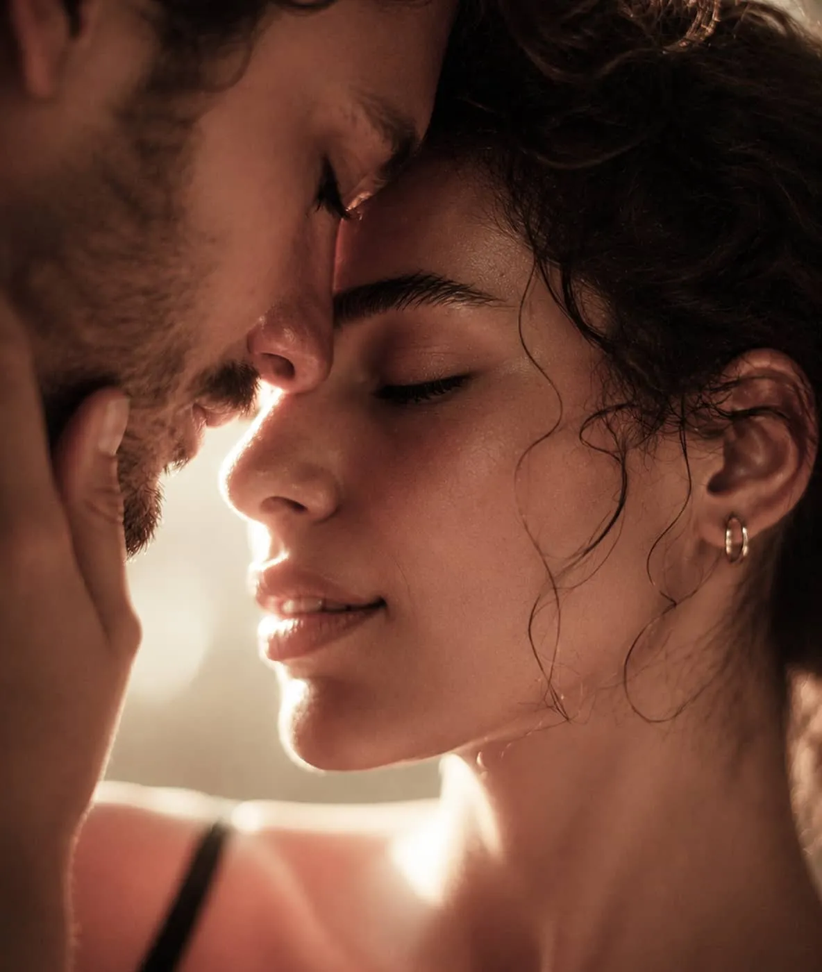 Close-up of a man and woman touching foreheads with eyes closed in an intimate moment.