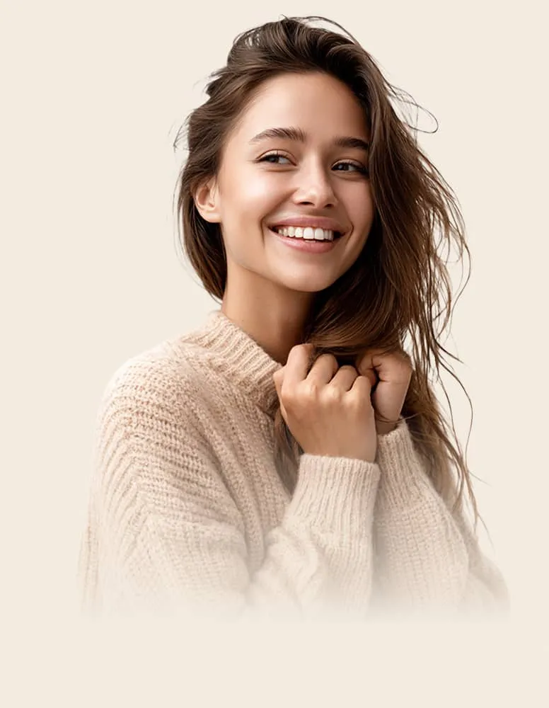Smiling young woman in a beige knit sweater with long brown hair looking to the side.