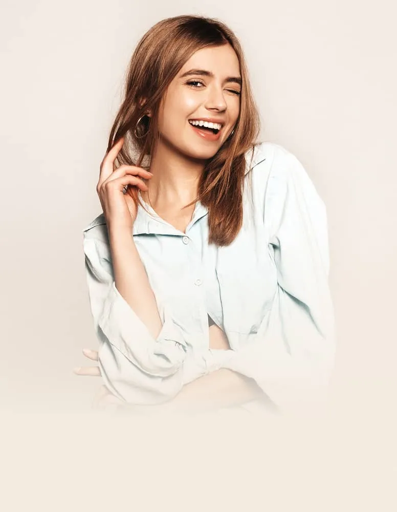 Young woman with brown hair winking and smiling wearing a light blue shirt against beige background.