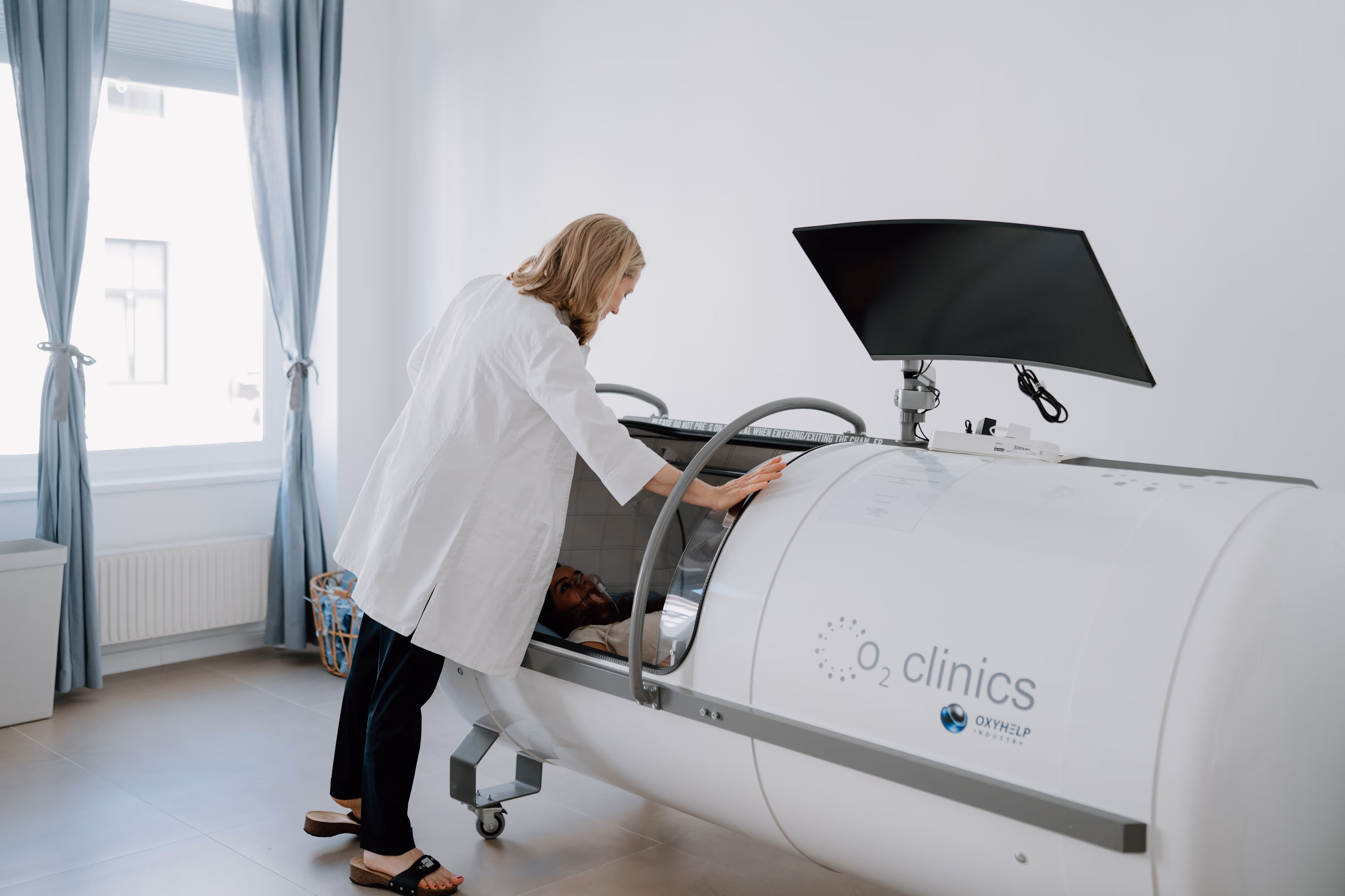 Ärztin überprüft Patient in O2 Klinik-Hyperbarik-Kammer im hellen Behandlungsraum.