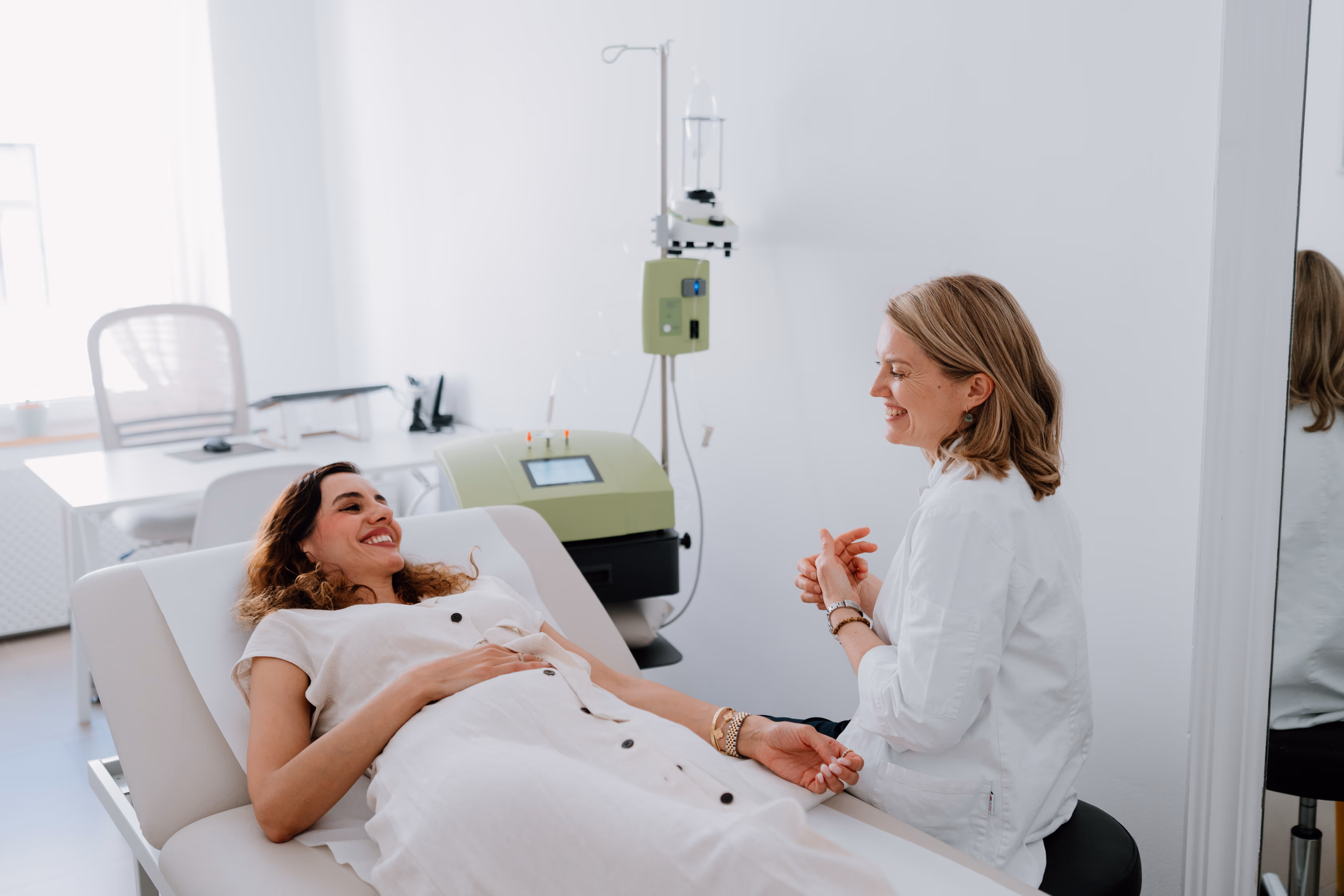 Patient lächelt und spricht mit einer medizinischen Fachkraft in einer hellen Behandlungszimmer.