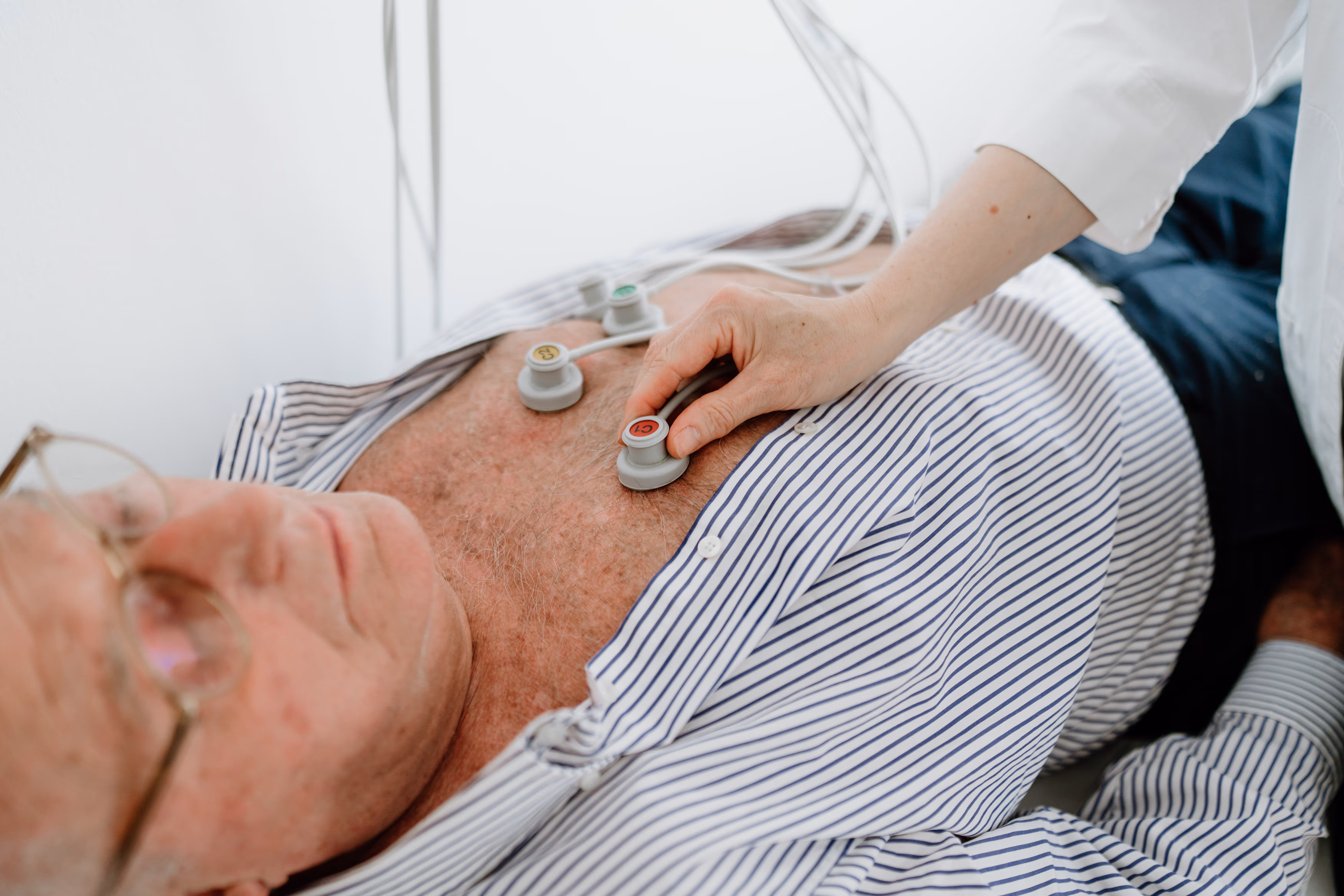 Arzt legt Elektroden für EKG am freigelegten Brustkorb eines älteren Patienten an.