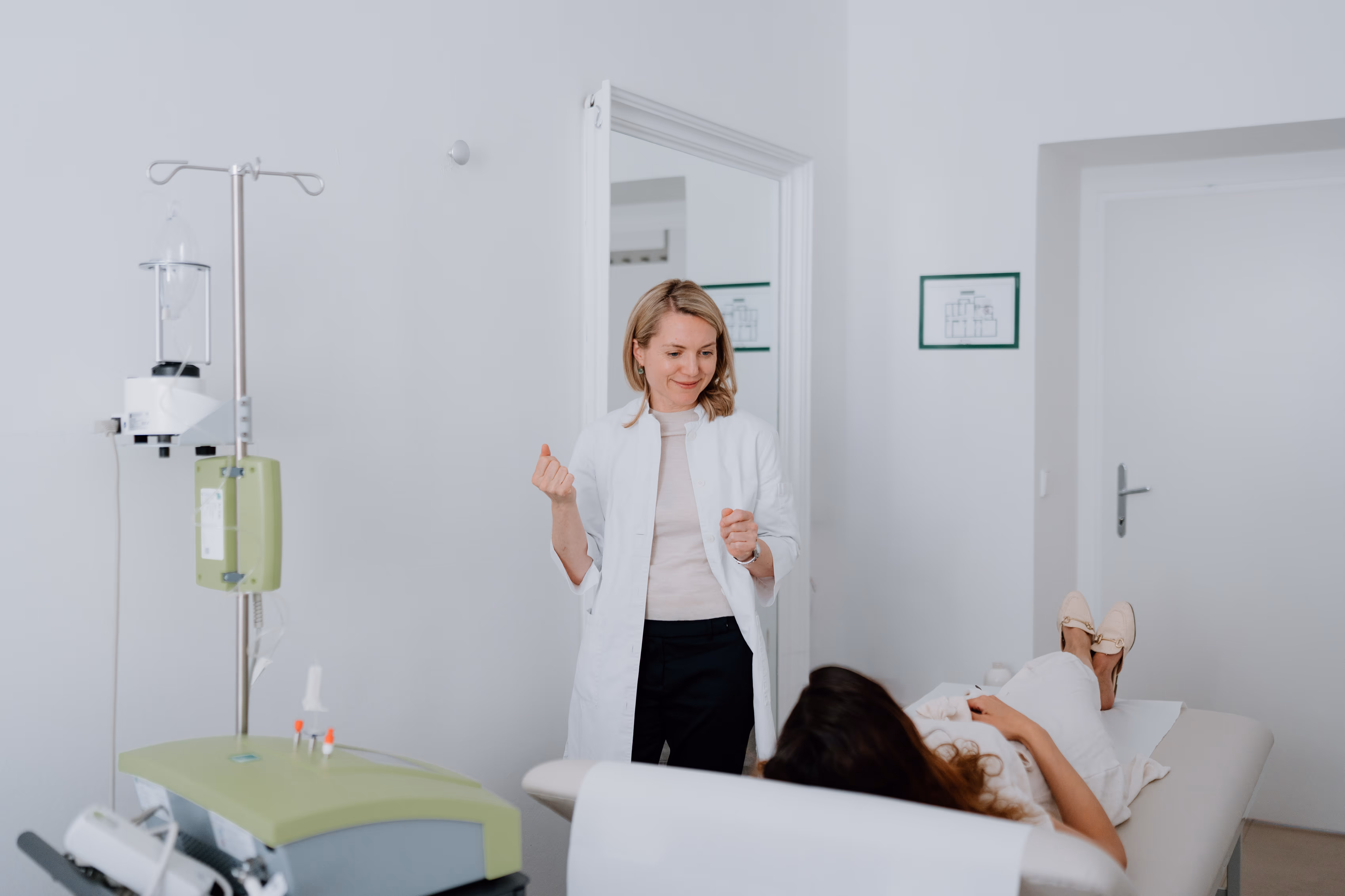 Ärztin in weißem Kittel spricht mit Patientin, die auf Behandlungsbank liegt in Praxis.