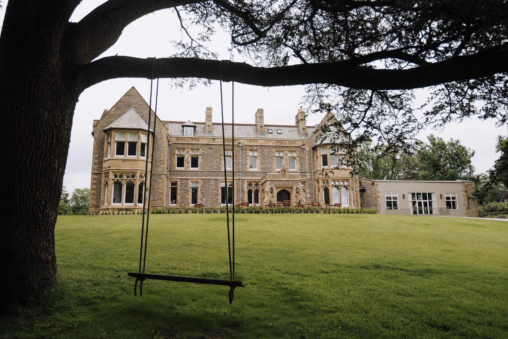Large historic stone mansion with a curved gravel driveway and green lawn with tall trees.