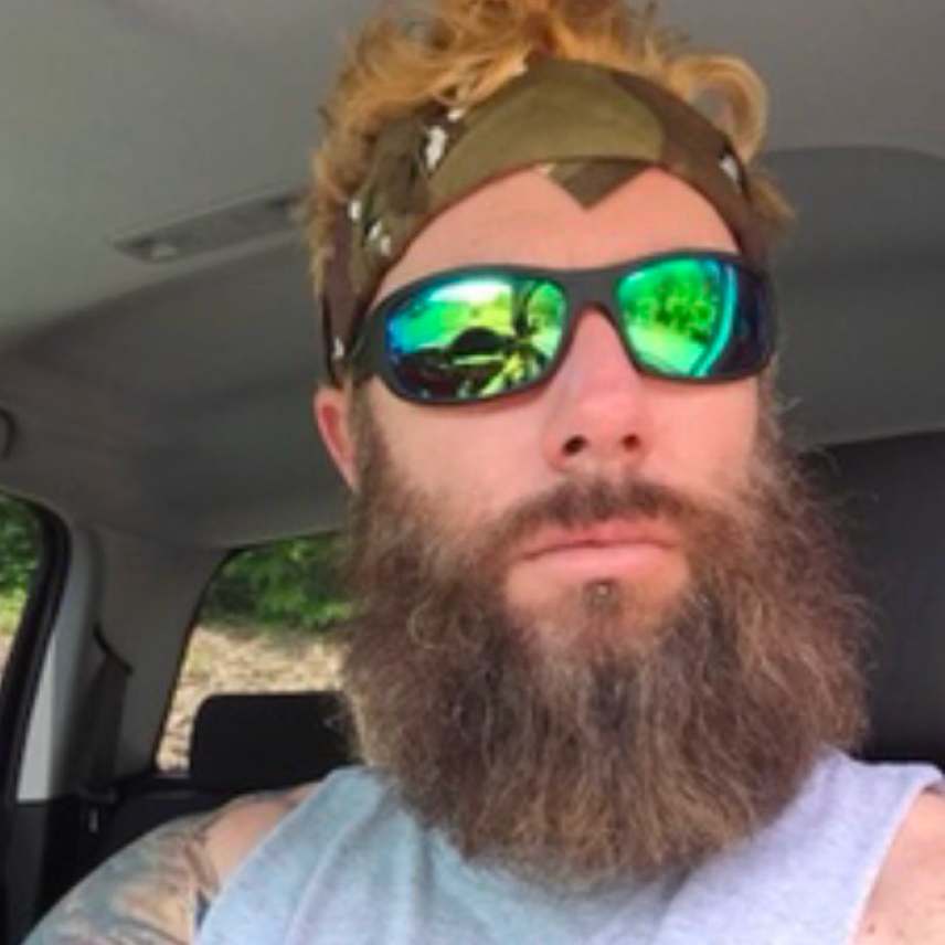 Bearded man wearing mirrored sunglasses and a green bandana sitting inside a vehicle.