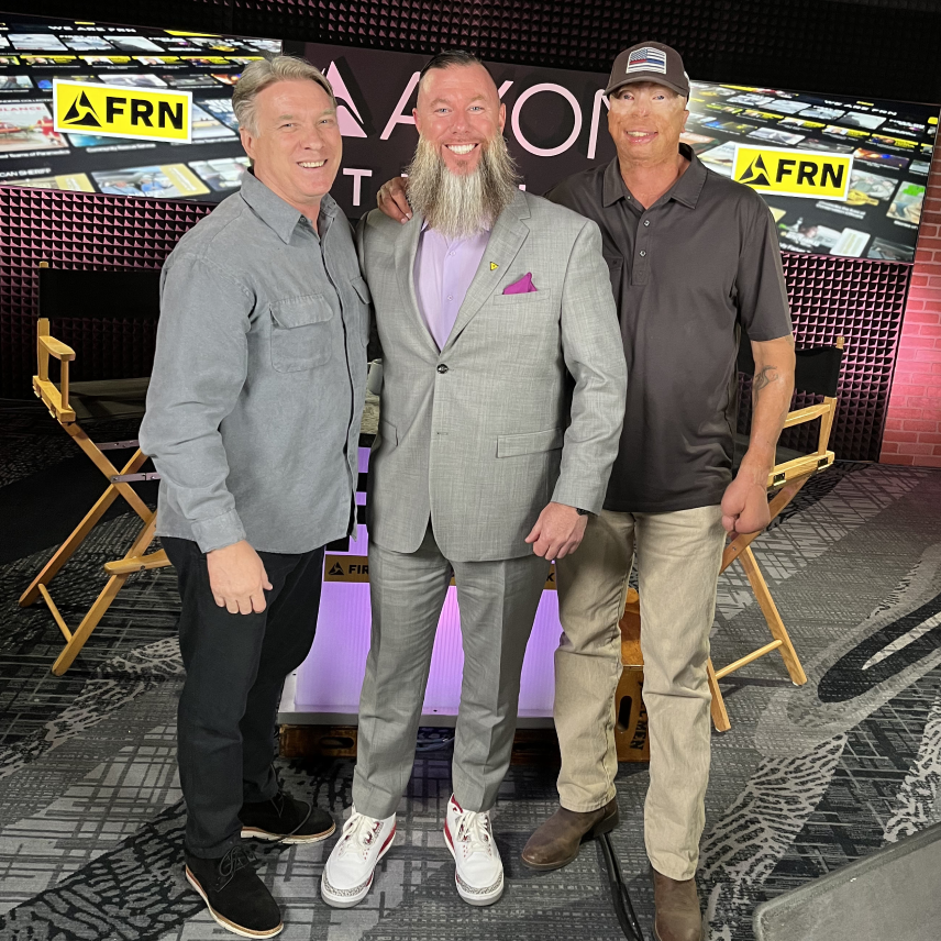 Three men posing smiling in a studio with FRN logos and director chairs behind them.