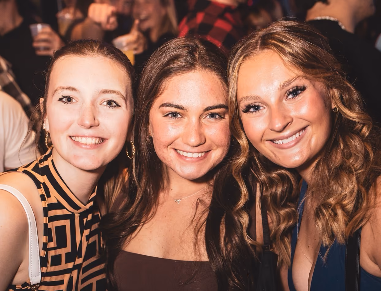 Three guests in patterned dresses posing together at a party at Dive Bar Cleveland.
